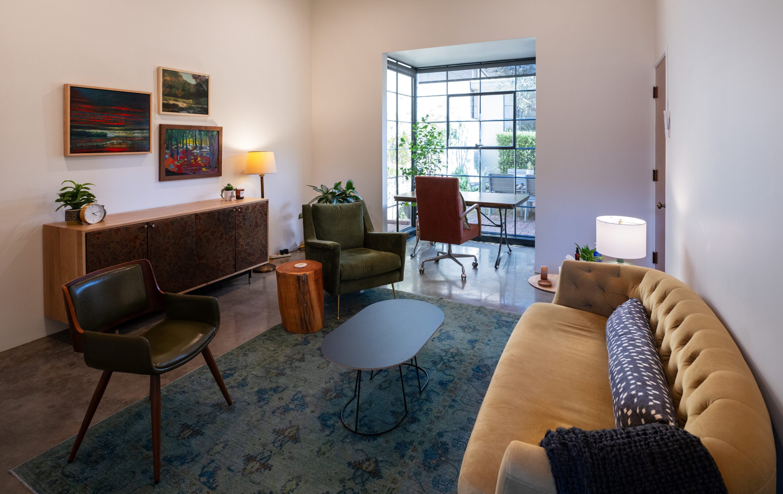 Living room with colorful paintings, a sofa, chairs, a coffee table, and a window with natural light.