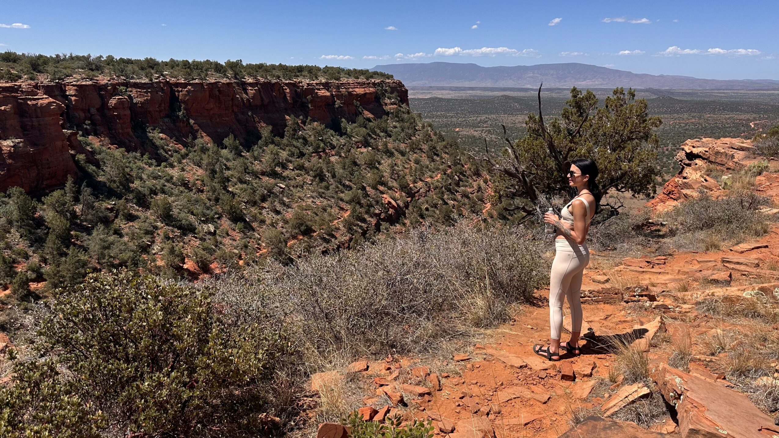 Woman standing on rocky terrain with a canyon and blue sky in the background.