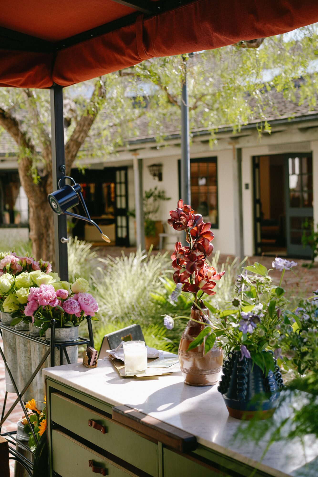 Outdoor scene with a table, flowers, and a building in the background, under a red canopy.