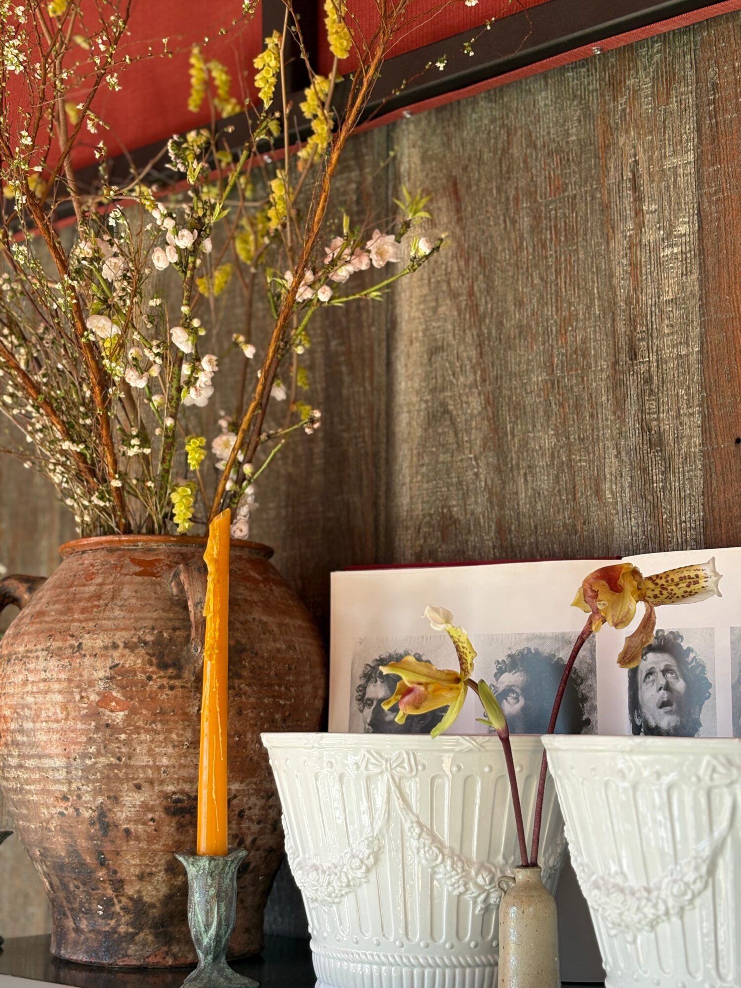 Vase with yellow and pink flowers, framed photo, and white decorative containers on a wooden surface.