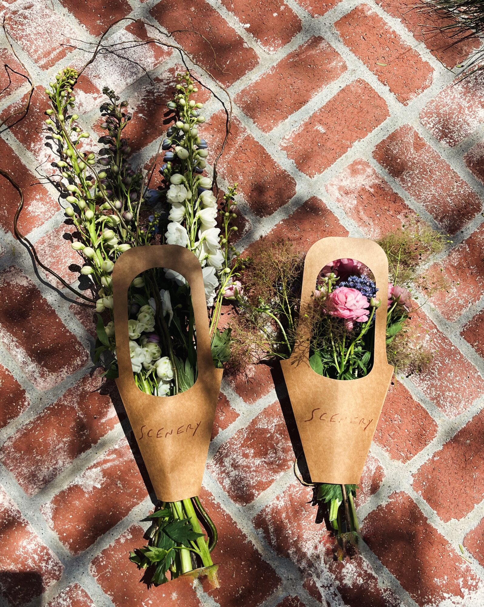 Two paper cones with flowers and greenery, hanging against a brick wall background.