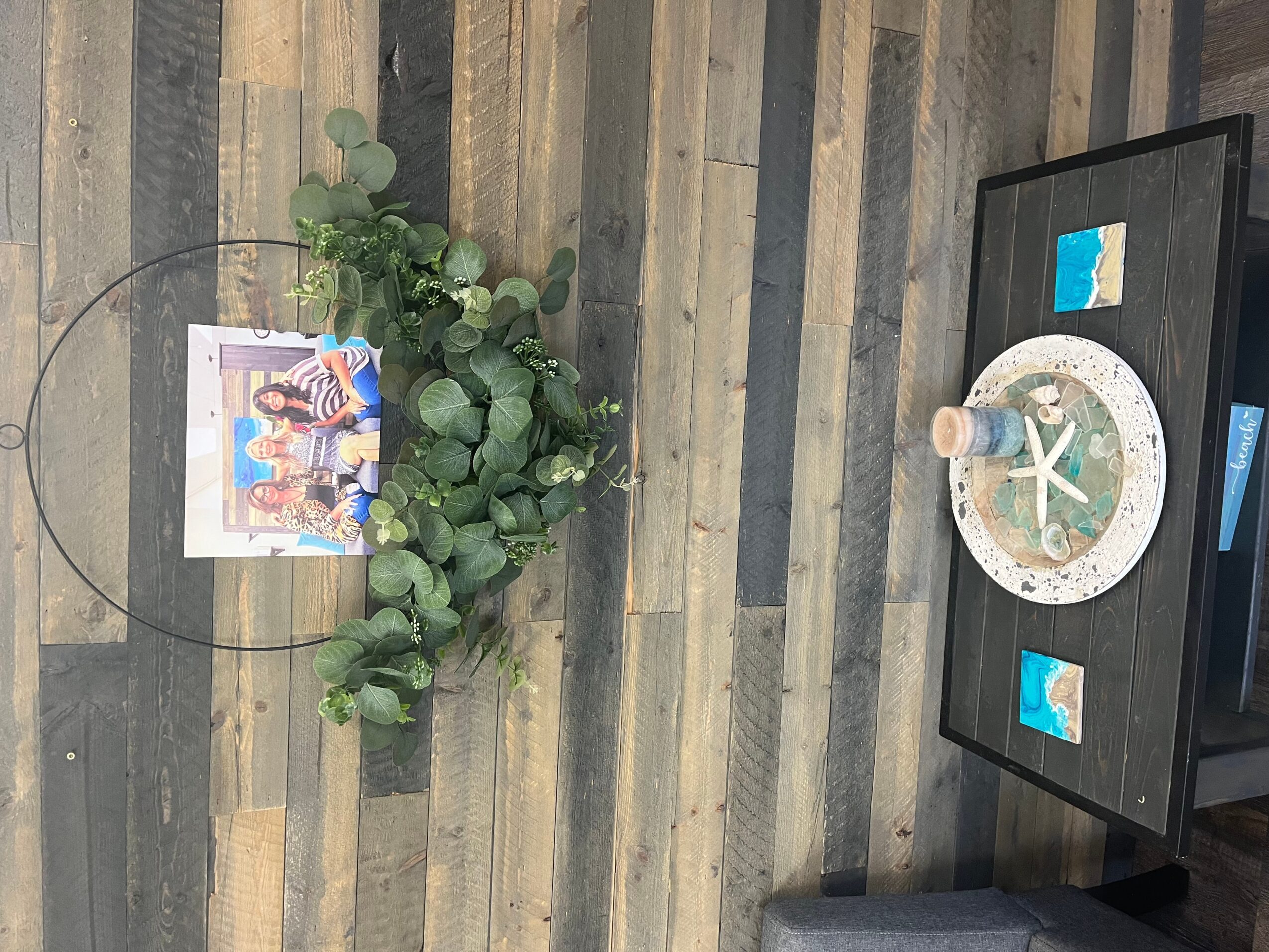 Decorative table with a lighthouse model, framed photo, and small blue and white objects, against a wooden wall.
