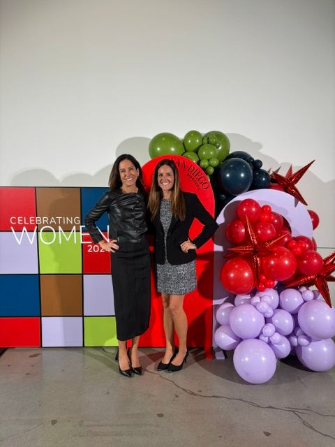 Two women stand in front of colorful balloons and a sign that says 'Celebrating Women 2023'.
