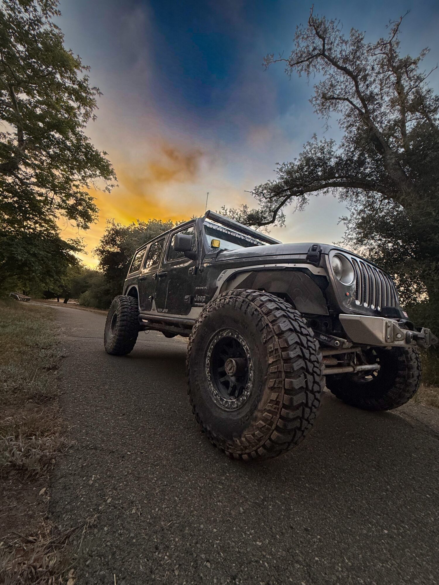 Off-road vehicle parked on a dirt path with trees and a sunset sky in the background.