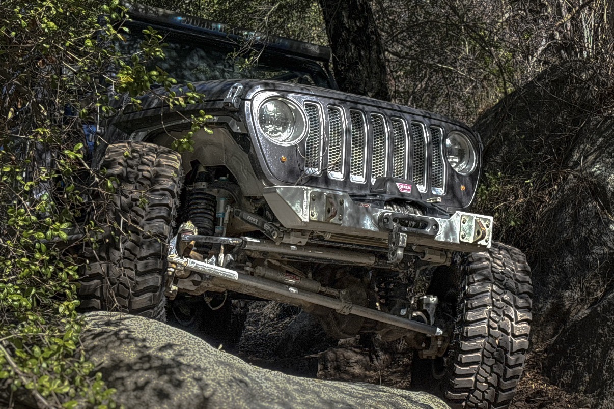 Off-road vehicle with large tires and a rugged front, parked among rocks and trees in a natural setting.