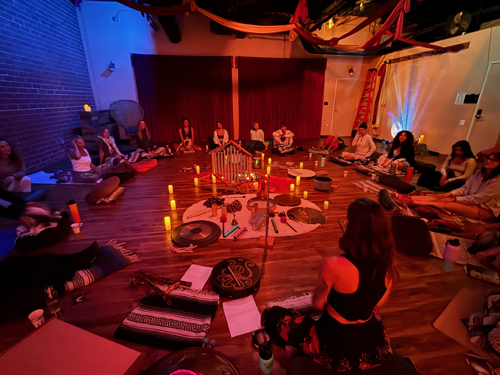 People sitting in a circle around a table with candles and decorations, in a dimly lit room with colorful lighting.