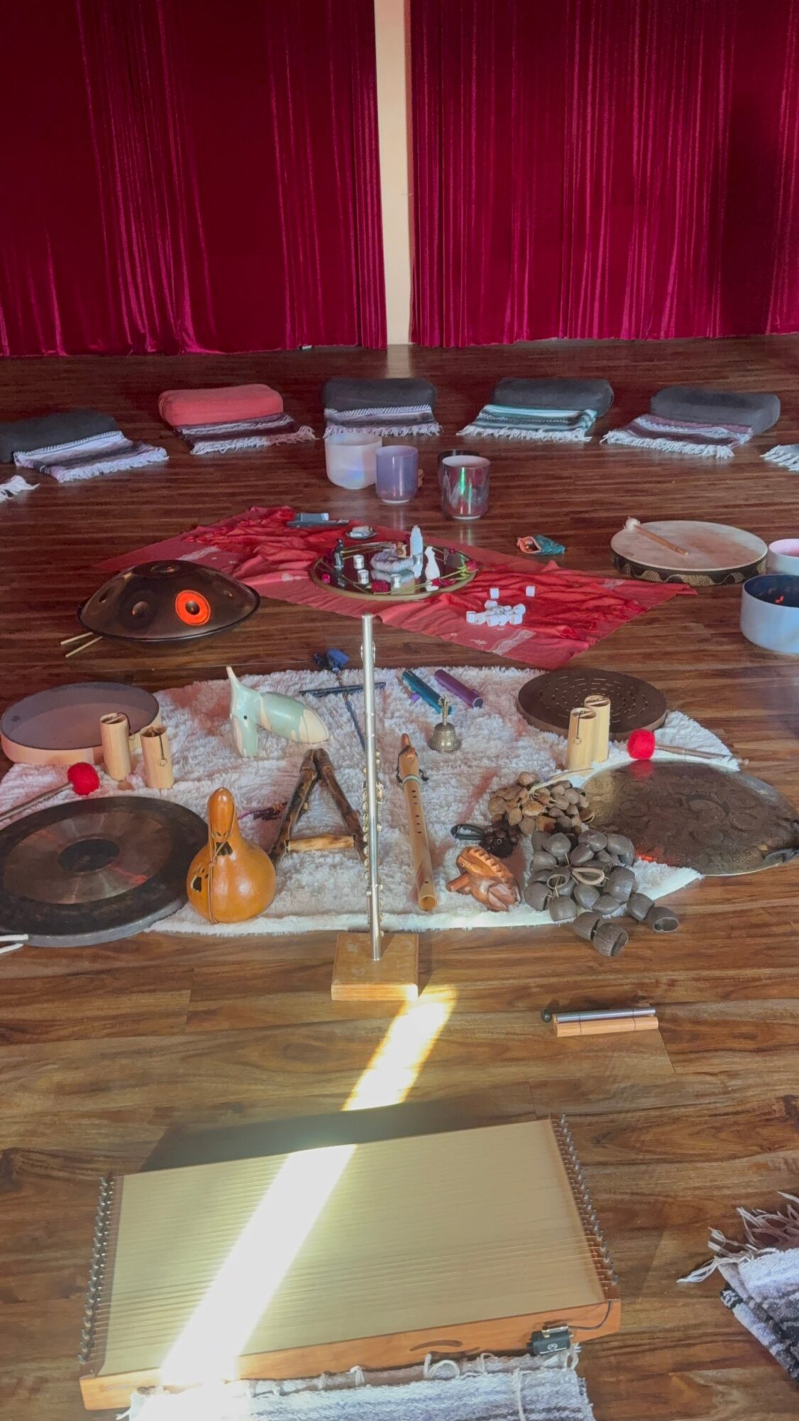 Arrangement of various objects on a wooden floor with red curtains in the background, including cloths, bowls, and decorative items.