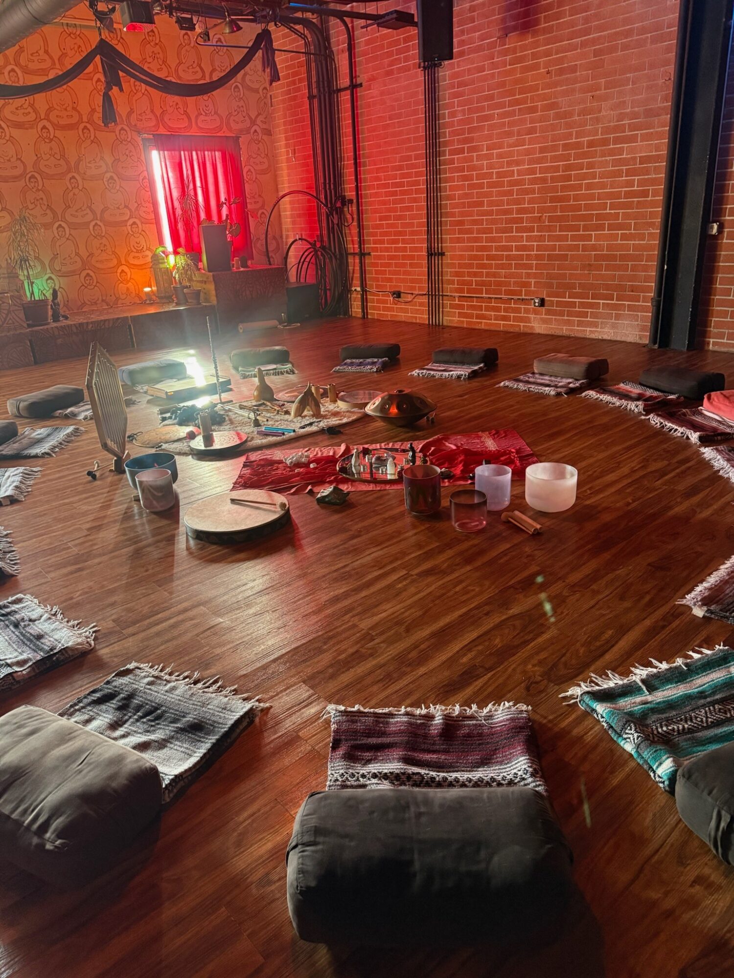 Indoor event space with a wooden floor, tables, chairs, and colorful lighting, decorated with drapes and string lights.