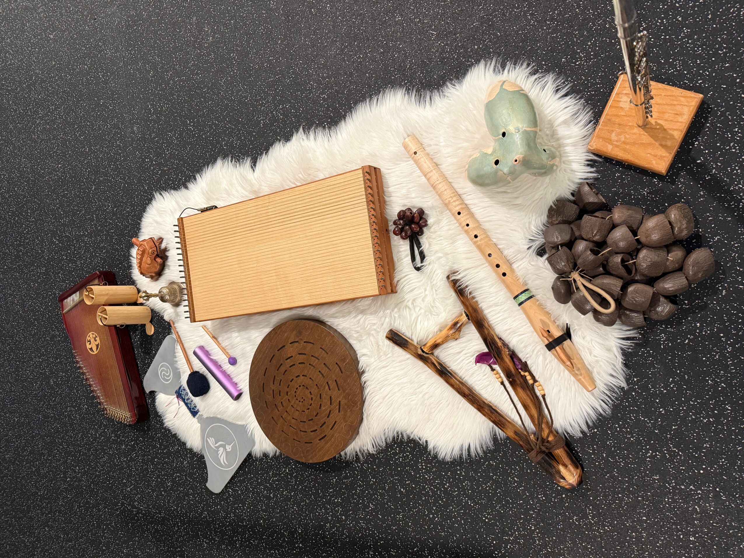 Collection of objects on a white furry surface, including a wooden box, a green ceramic object, rocks, and sticks.