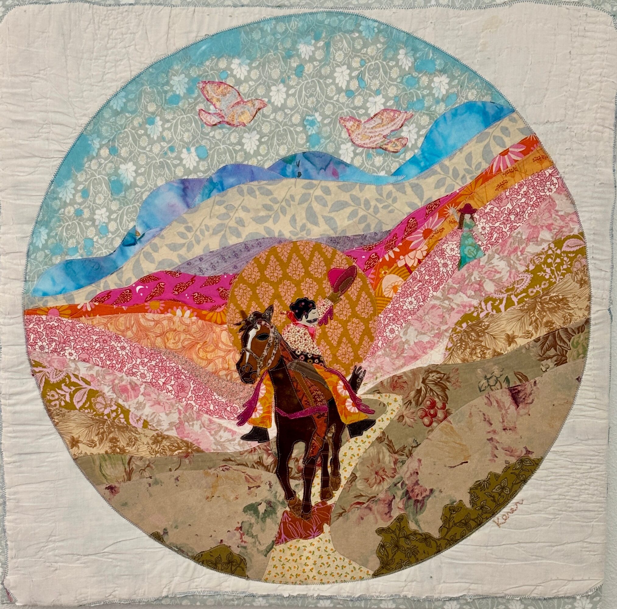Colorful circular textile art depicting a person riding a horse in a landscape with mountains, birds, and patterned sky.