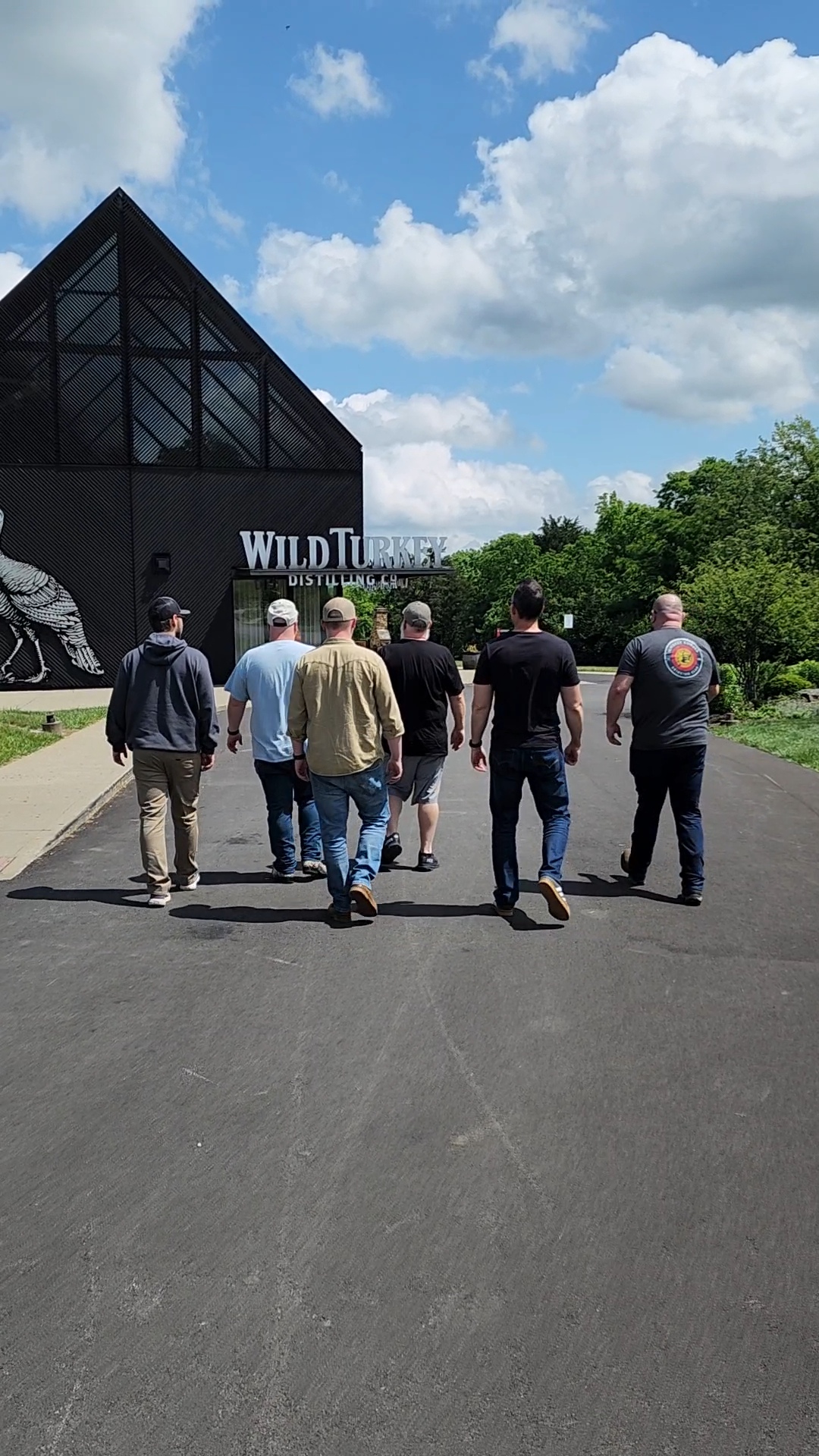 Group of seven people walking towards a building with a glass pyramid roof, trees, and a partly cloudy sky.