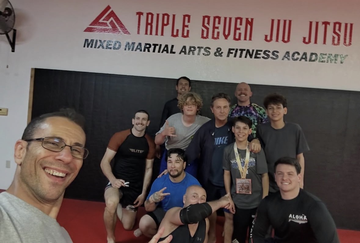 Group of people posing for a photo in a martial arts gym, with a man taking a selfie in the foreground.