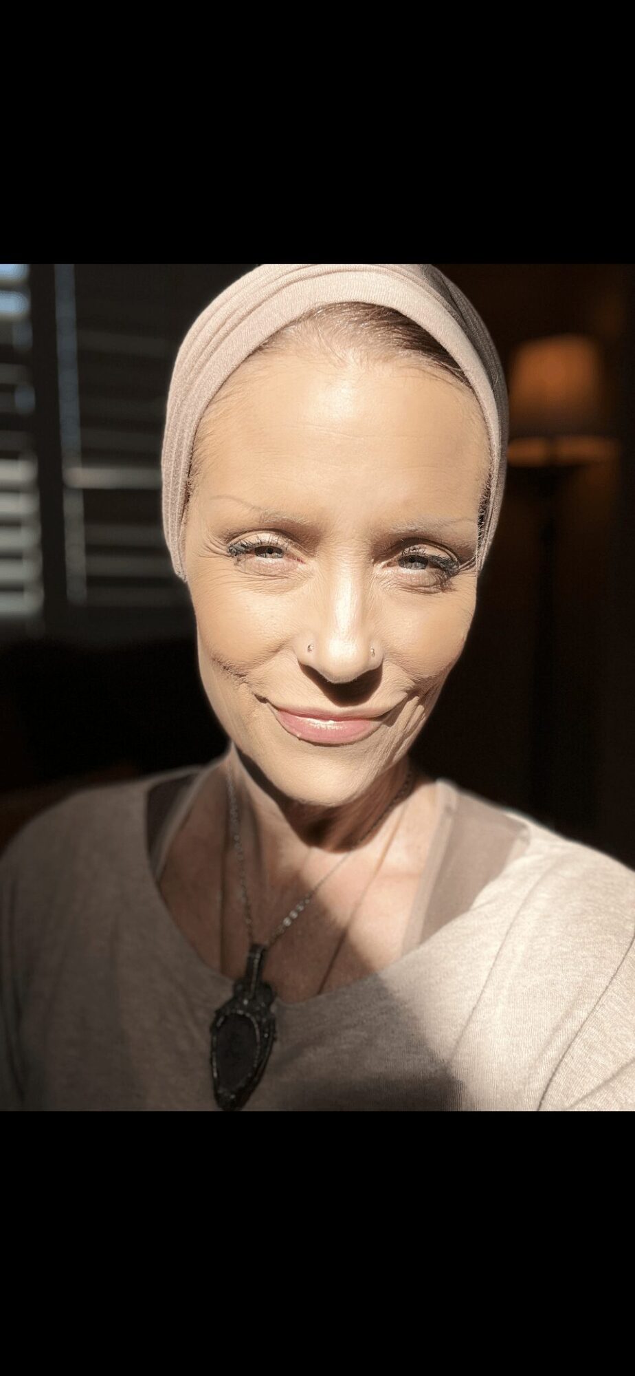Woman with light headscarf smiling, indoor background with lamp, close-up portrait, natural lighting.