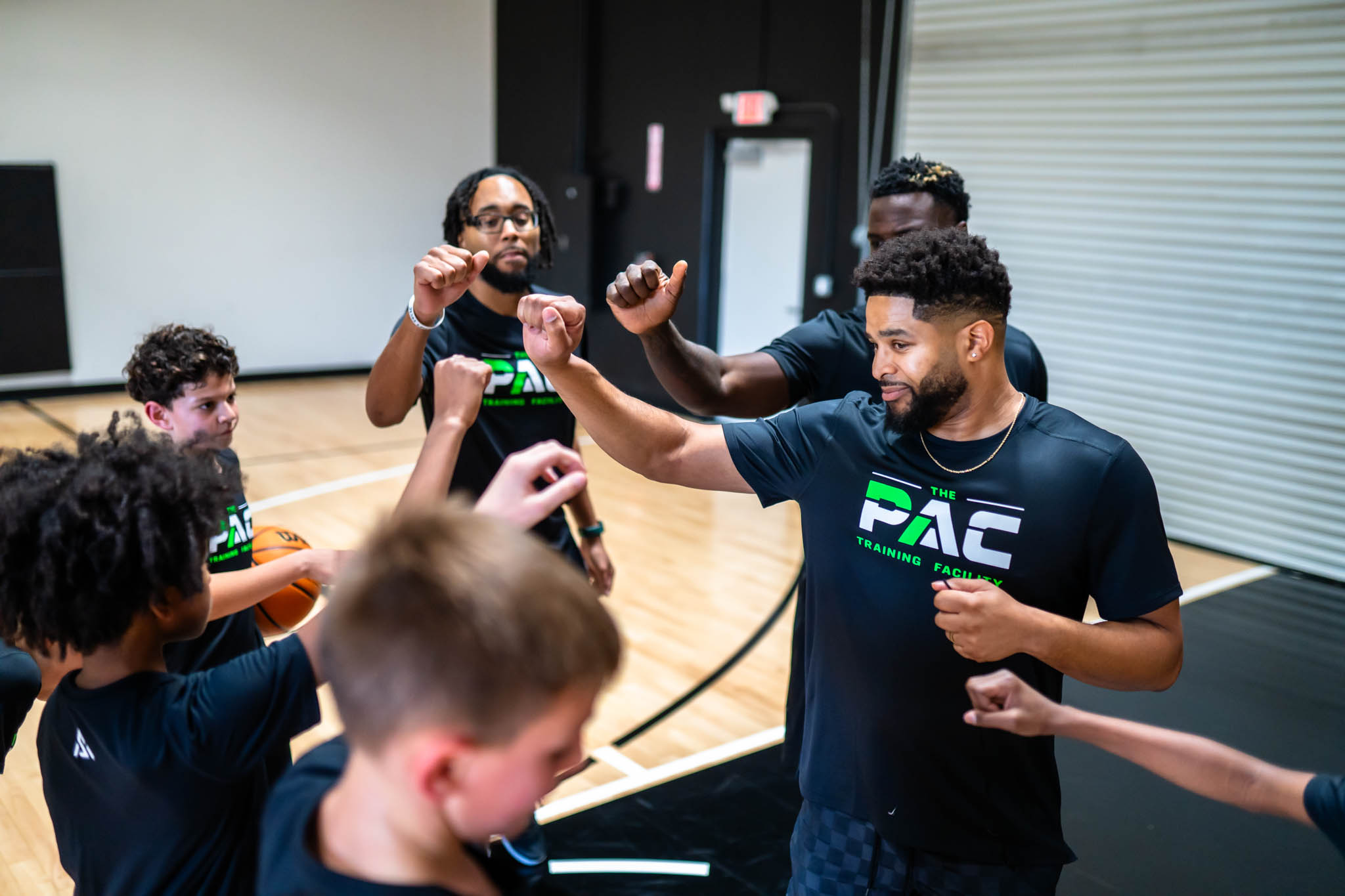 Group of people dancing and celebrating indoors, some with raised fists, wearing matching black shirts with green and white text.