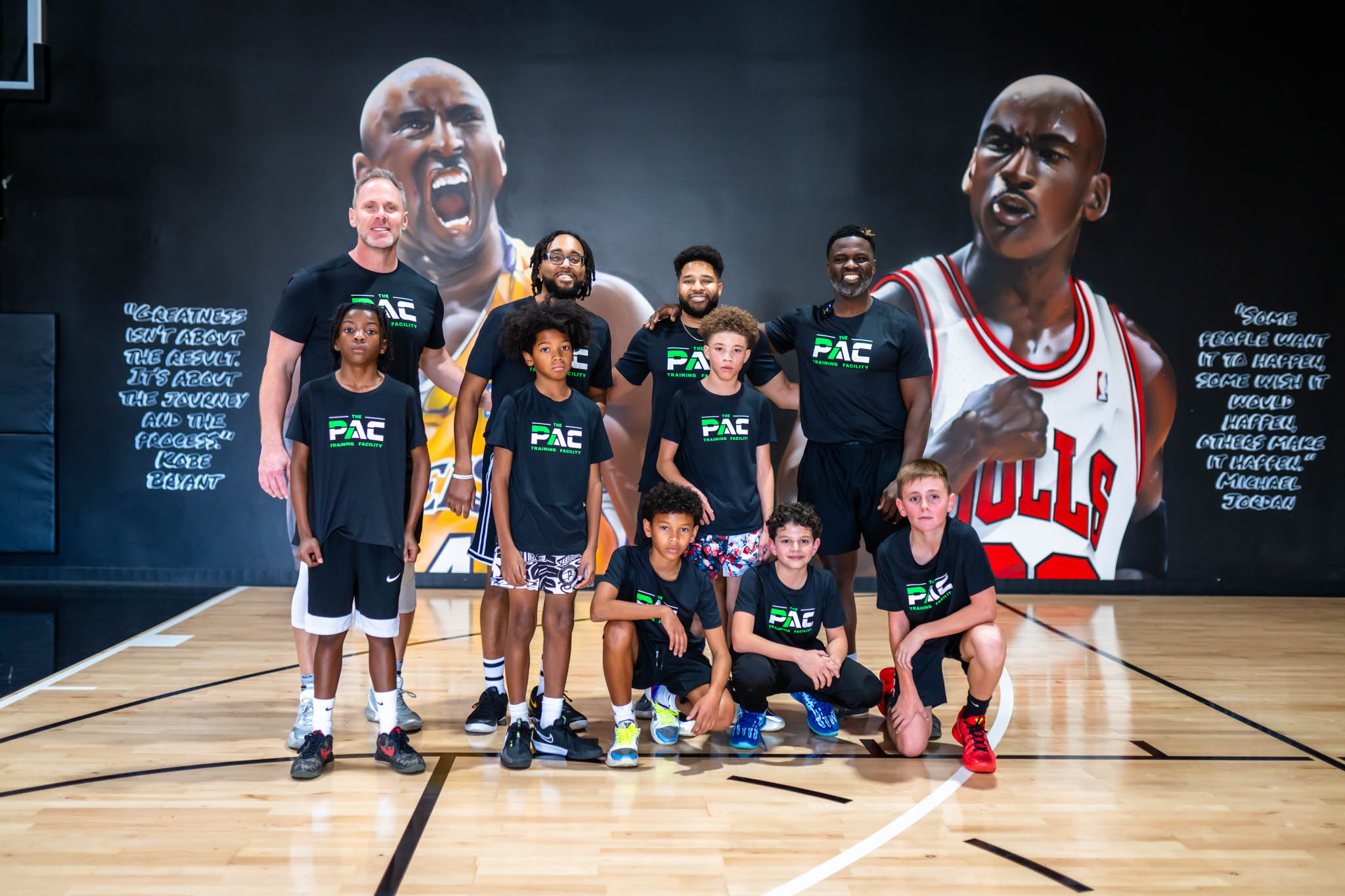 Group of young basketball players and coach posing on court with large Chicago Bulls mural in background.