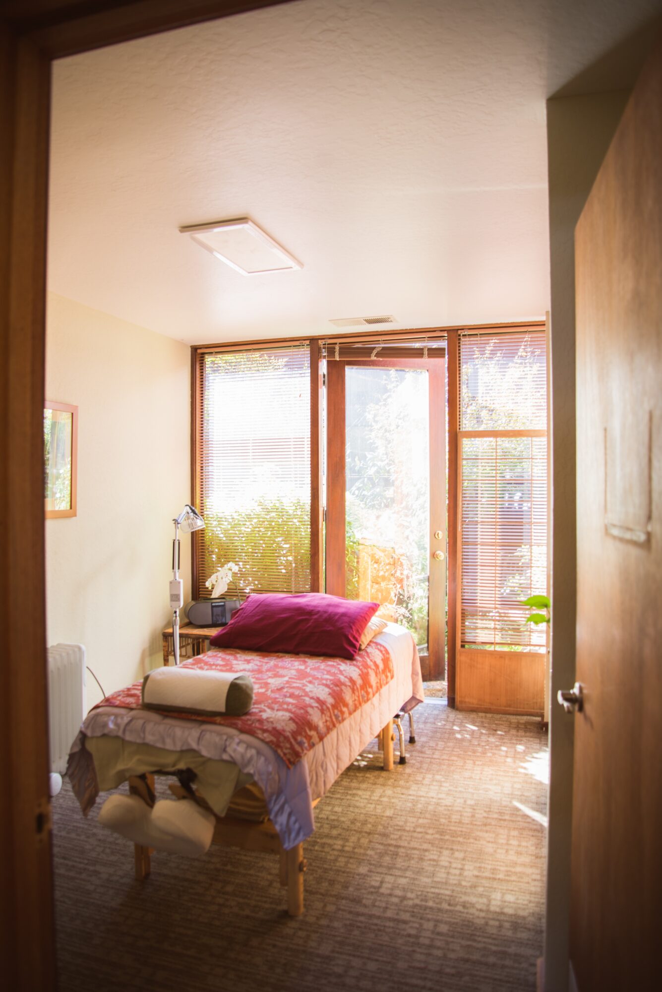 Small bedroom with bed, window, and door, sunlight streaming in, cozy and simple decor.