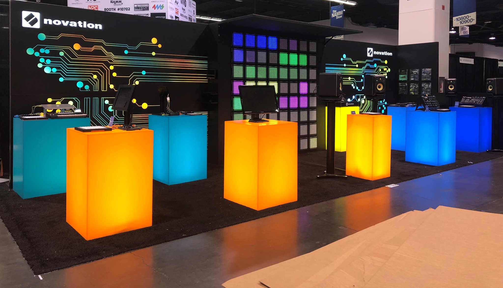 Colorful illuminated display booths with glowing cubes in orange, blue, and yellow at a technology exhibition.