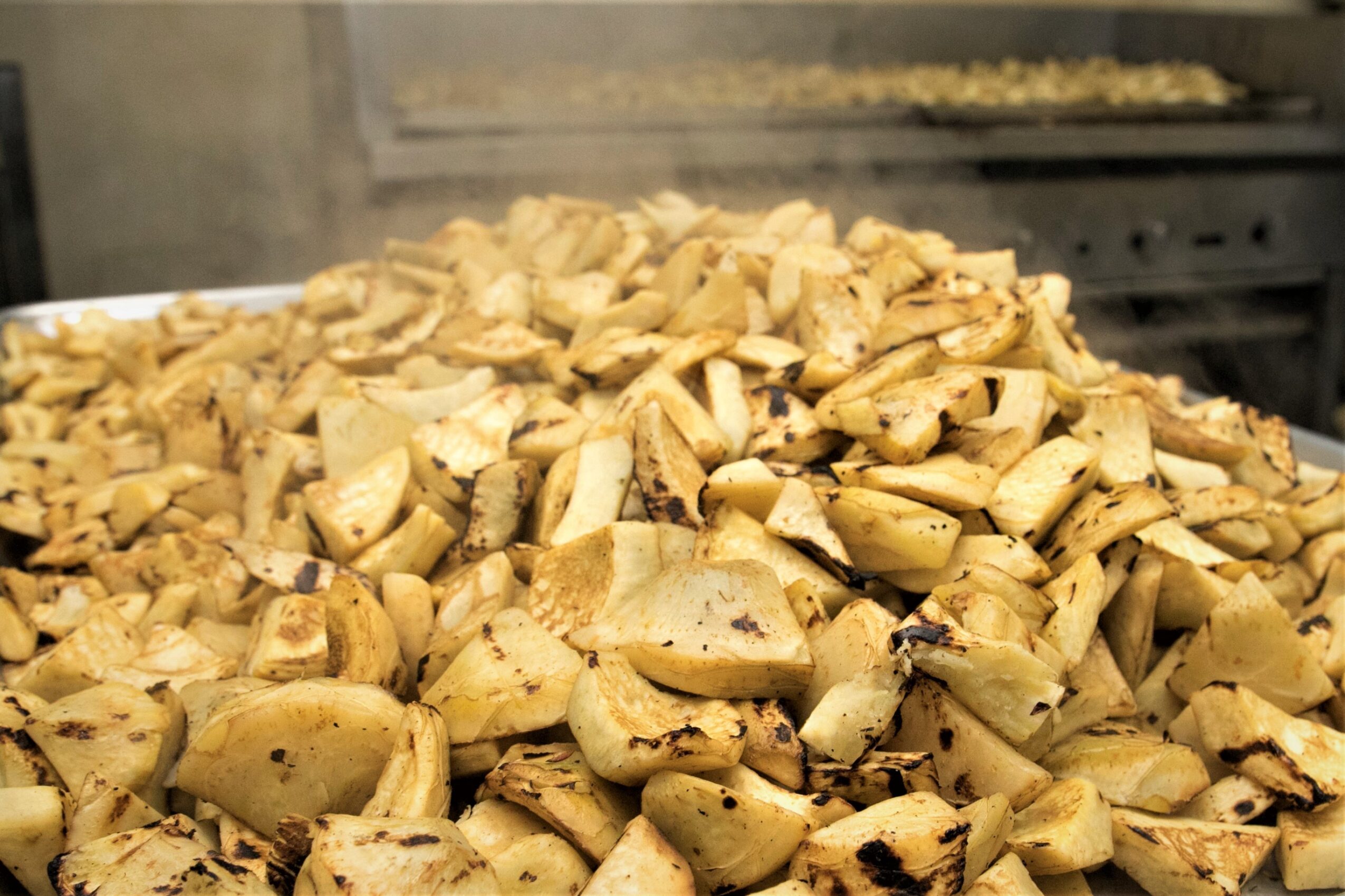 Cooked chopped vegetables, possibly potatoes or yams, steaming on a tray in a kitchen setting.