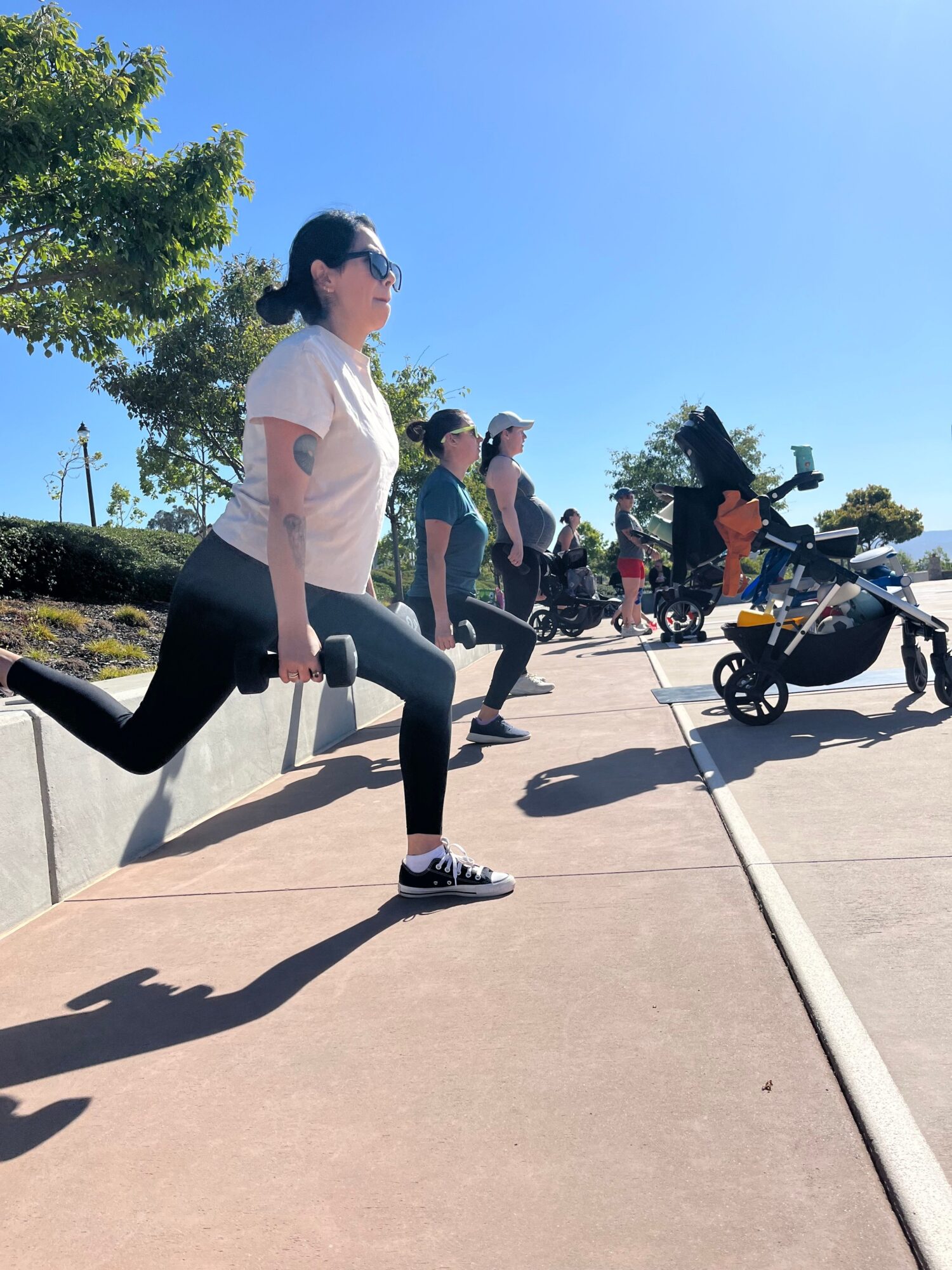 Person walking on sidewalk with group of people and bicycles in background, trees and blue sky, sunny day.