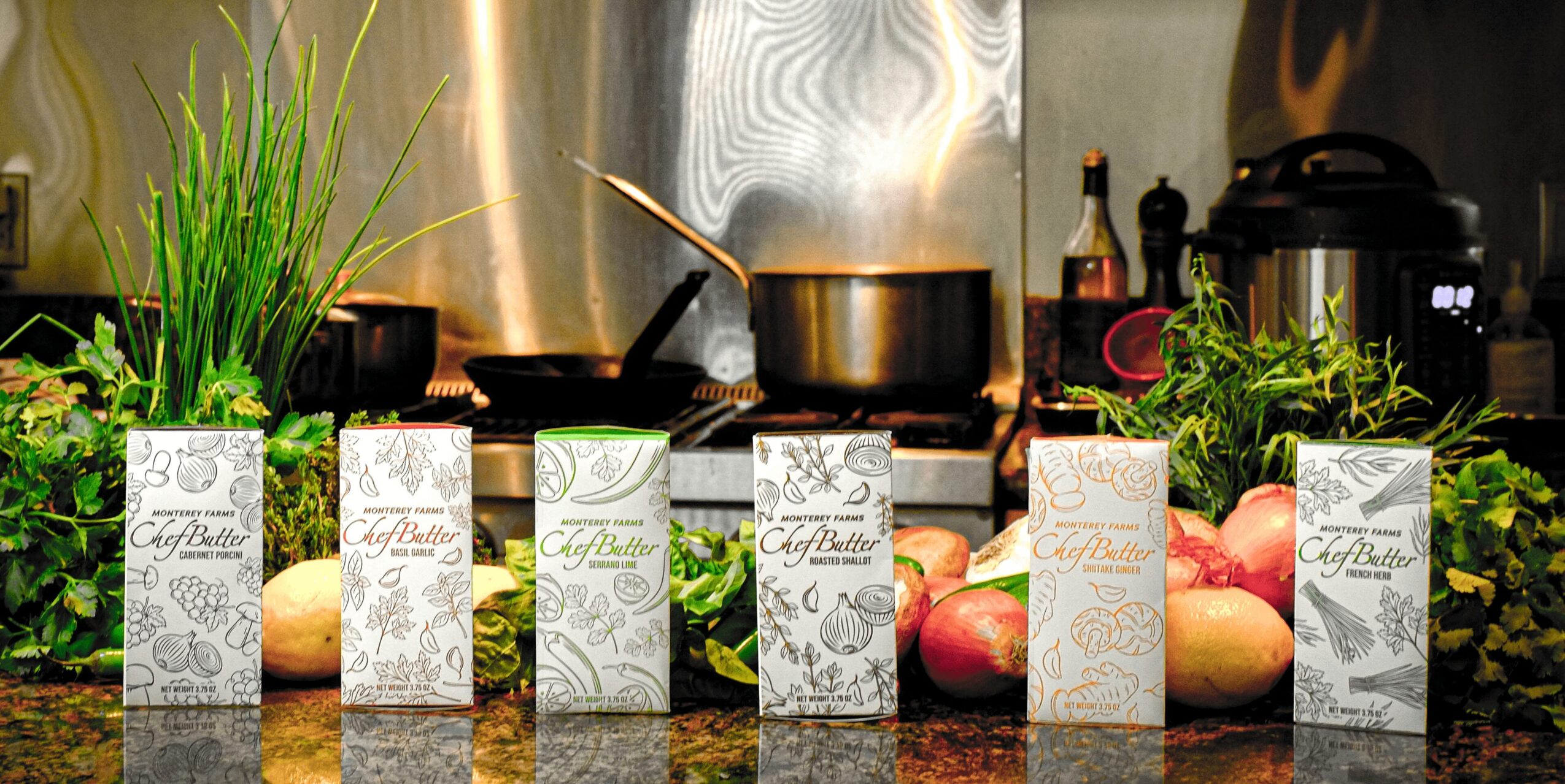 Kitchen countertop with six cartons, apples, and green plants, with cooking utensils and appliances in the background.