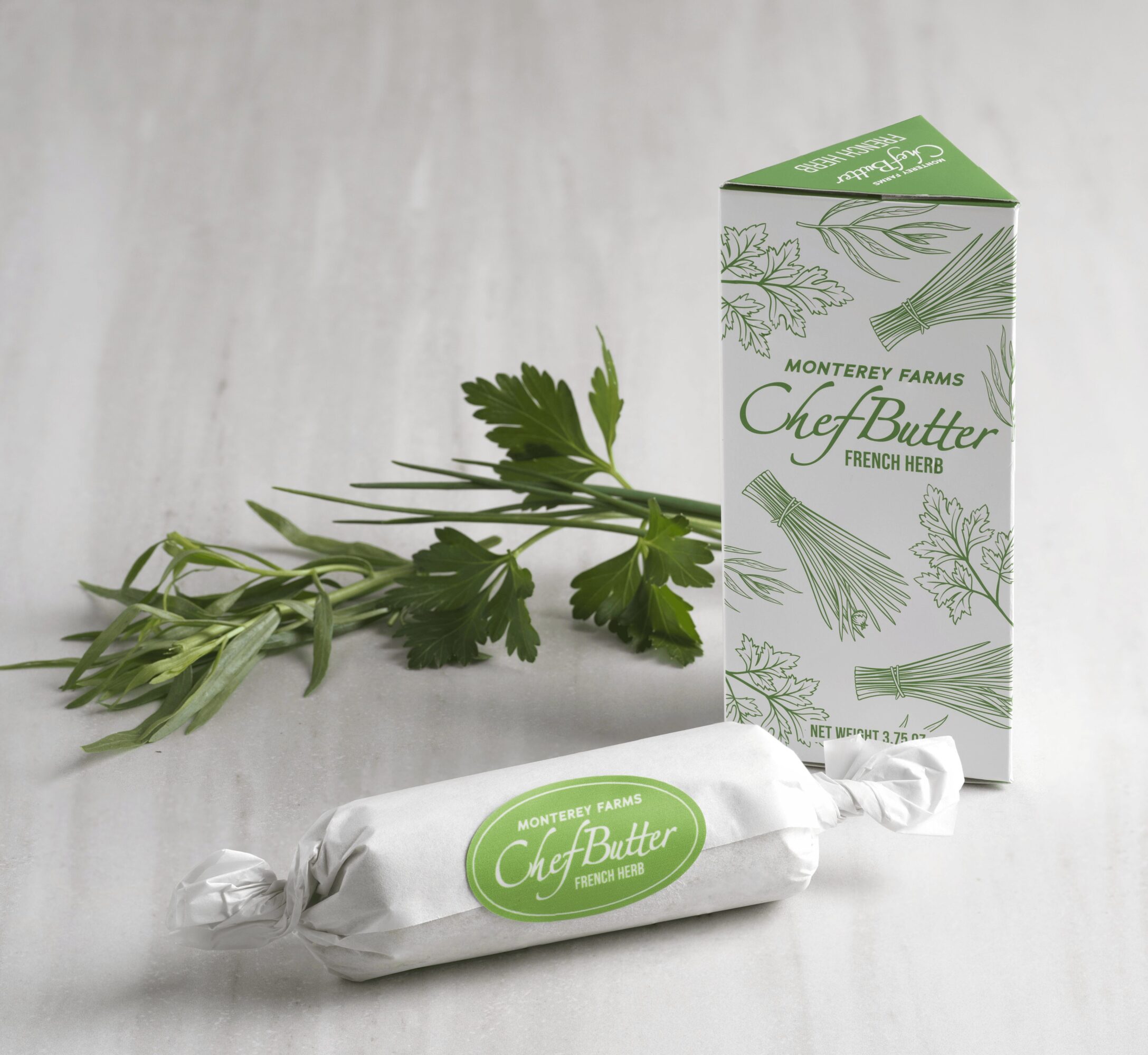 Fresh herbs, a wrapped butter package, and a carton box on a light surface.