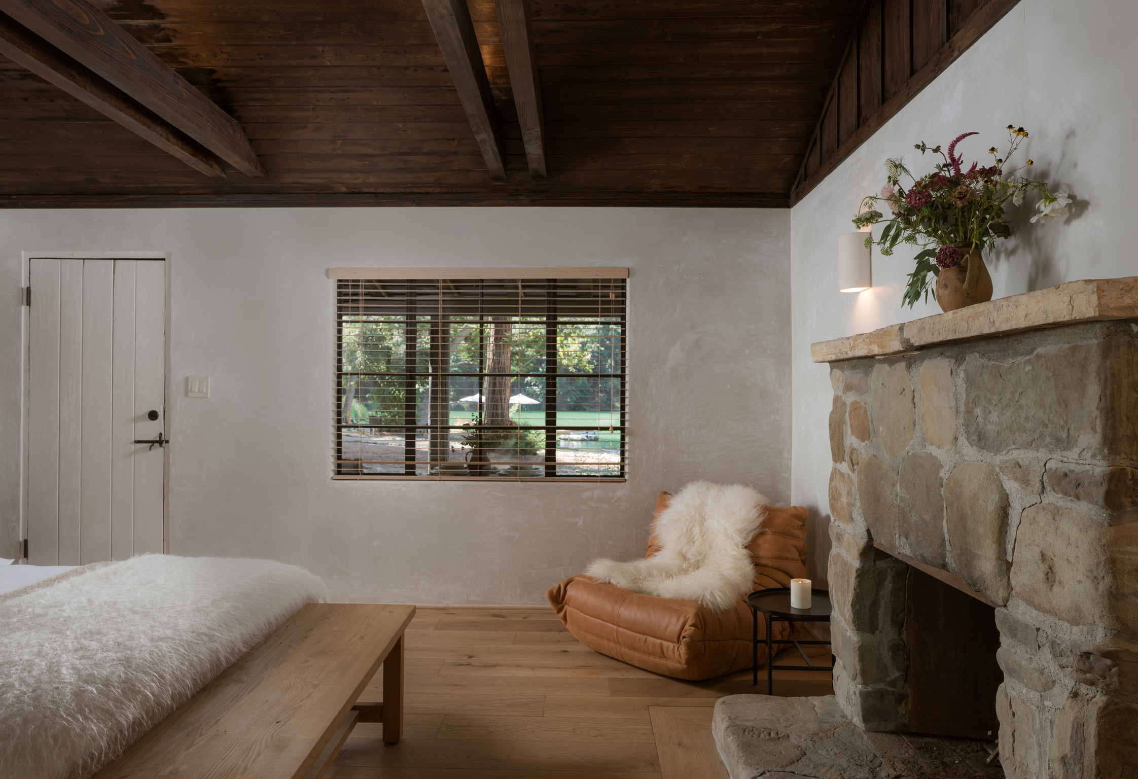 Living room with a window, stone fireplace, and a cozy chair with a sheepskin throw.