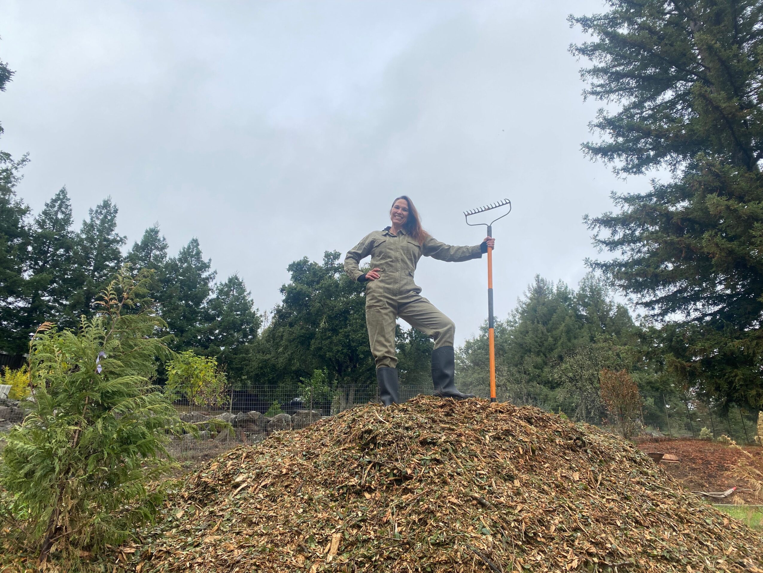 Person using a pickaxe outdoors on a dirt path surrounded by trees and greenery.
