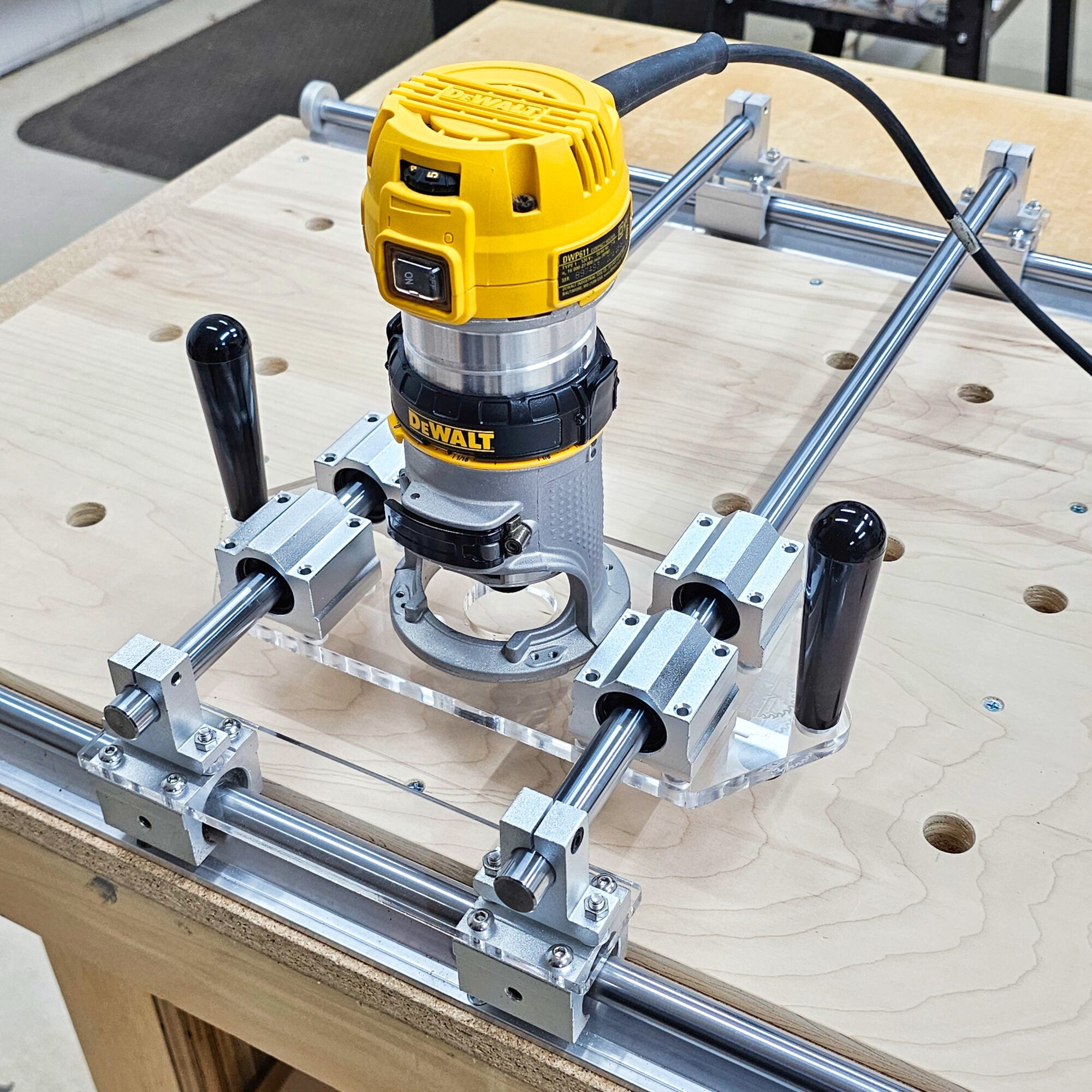 Yellow router mounted on a woodworking jig on a workbench, with black handles and metal rails, in a workshop setting.