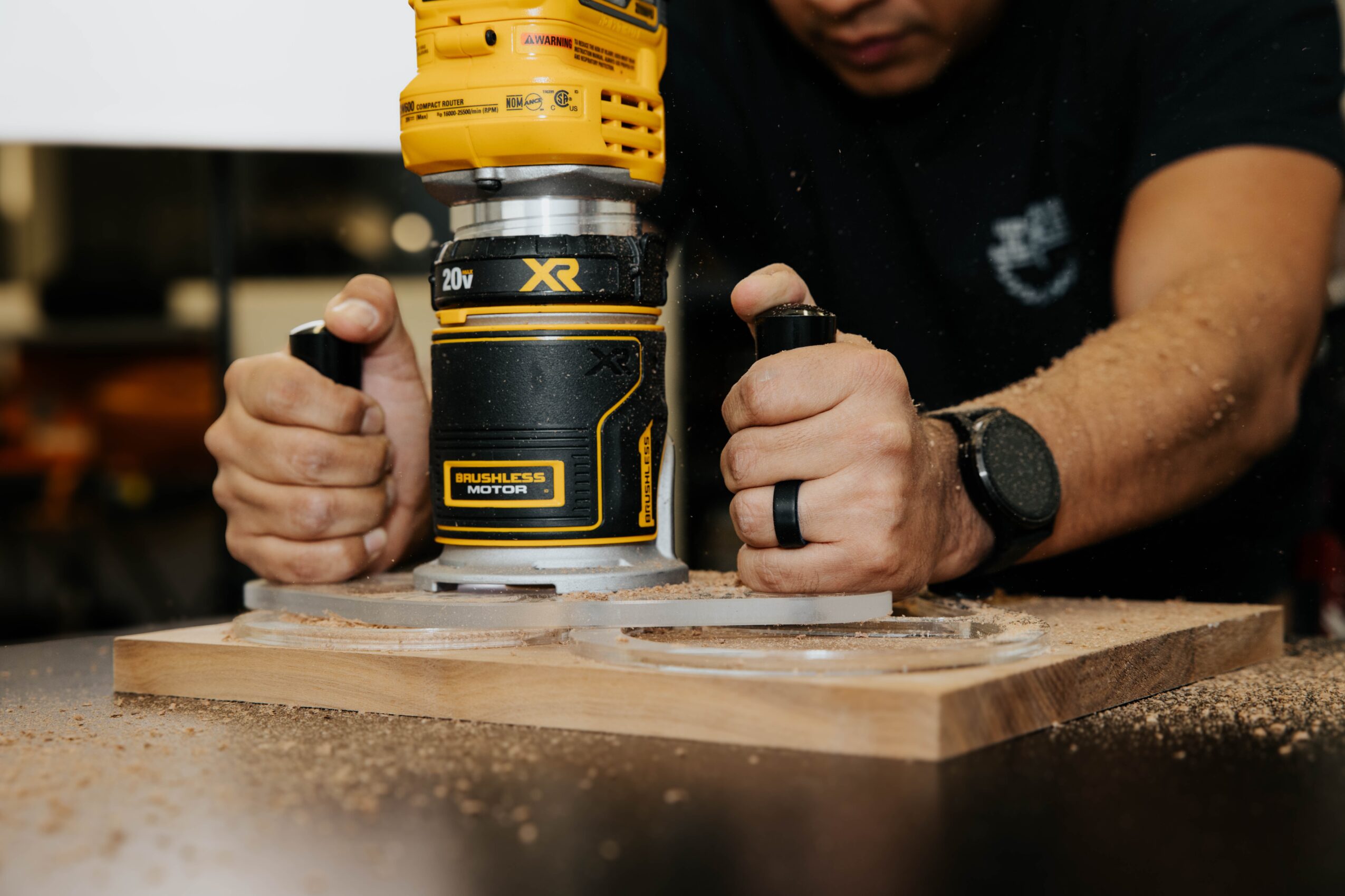 Person using a yellow power drill on a wooden surface, with hands gripping the drill and a watch on the wrist.