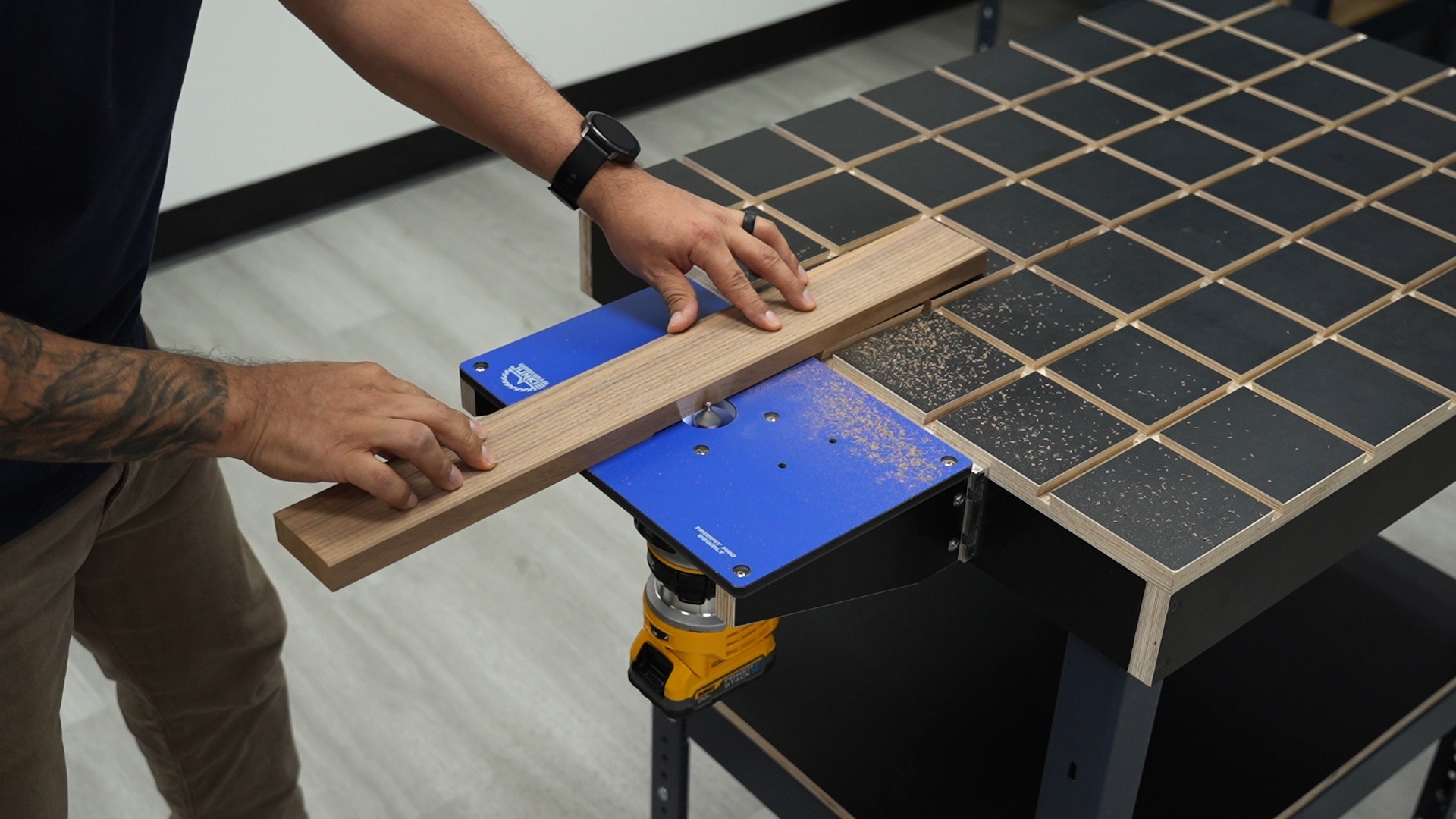 Person using a hand saw to cut a wooden board on a blue workbench in a workshop.