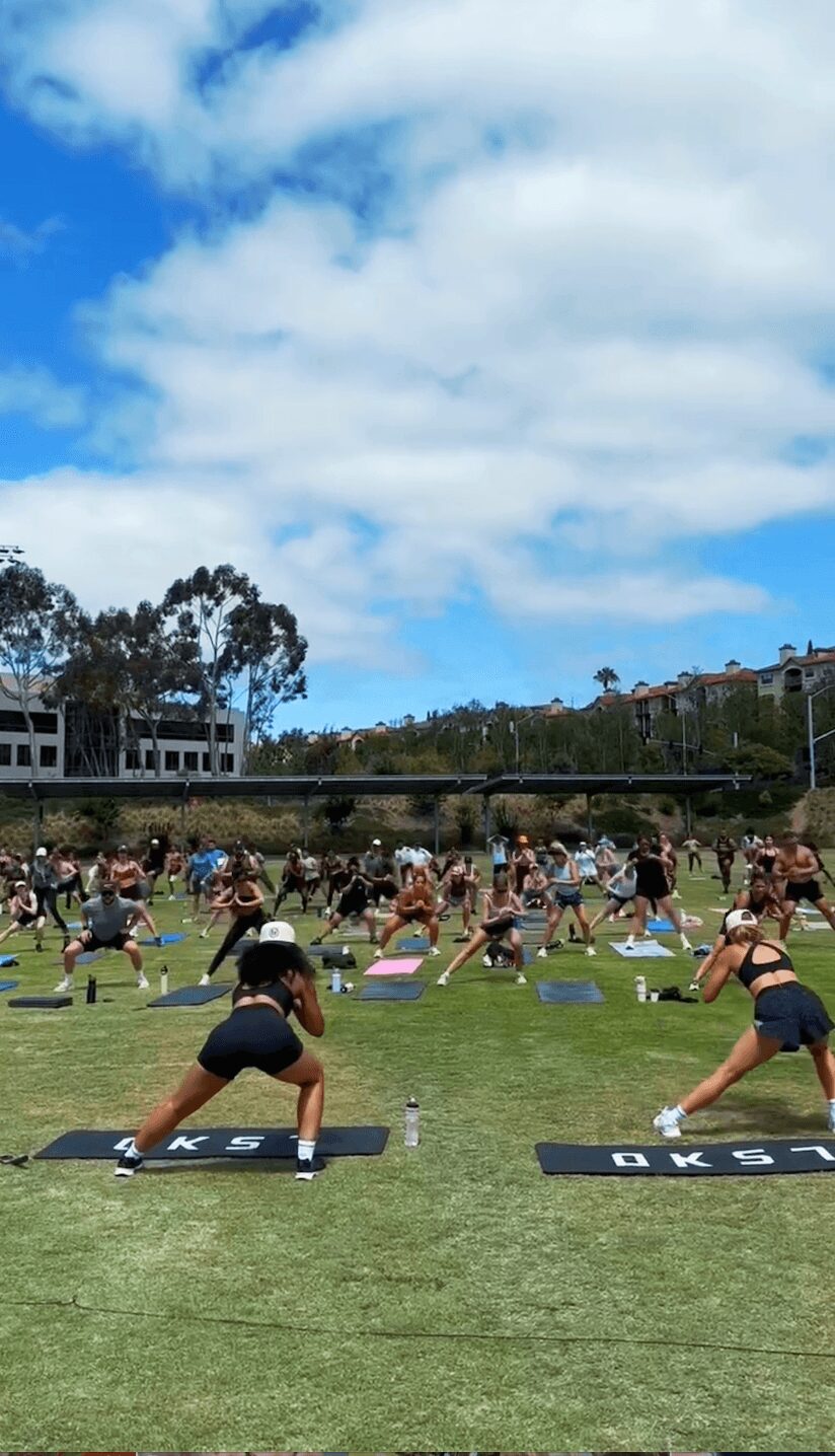 Group of people practicing yoga outdoors on mats in a grassy field under a partly cloudy sky.