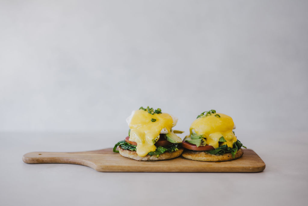 Two open-faced sandwiches on a wooden board with melted cheese, greens, and tomato slices.