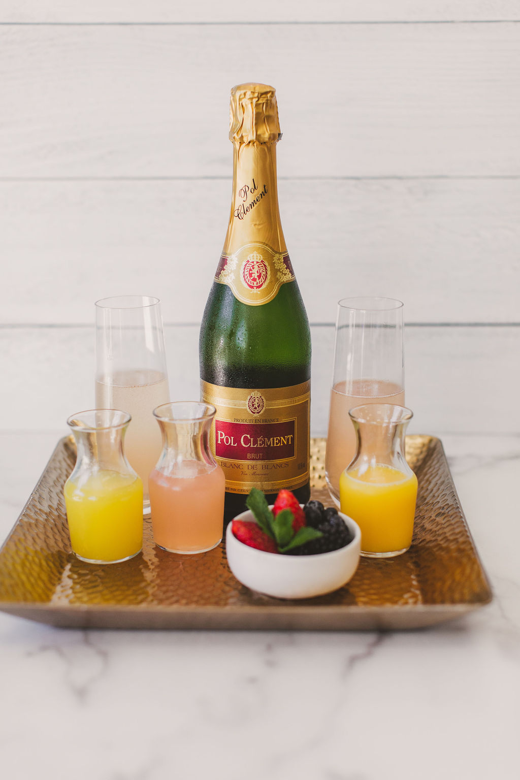 Champagne bottle with four glasses and a bowl of strawberries on a tray, on a white background.