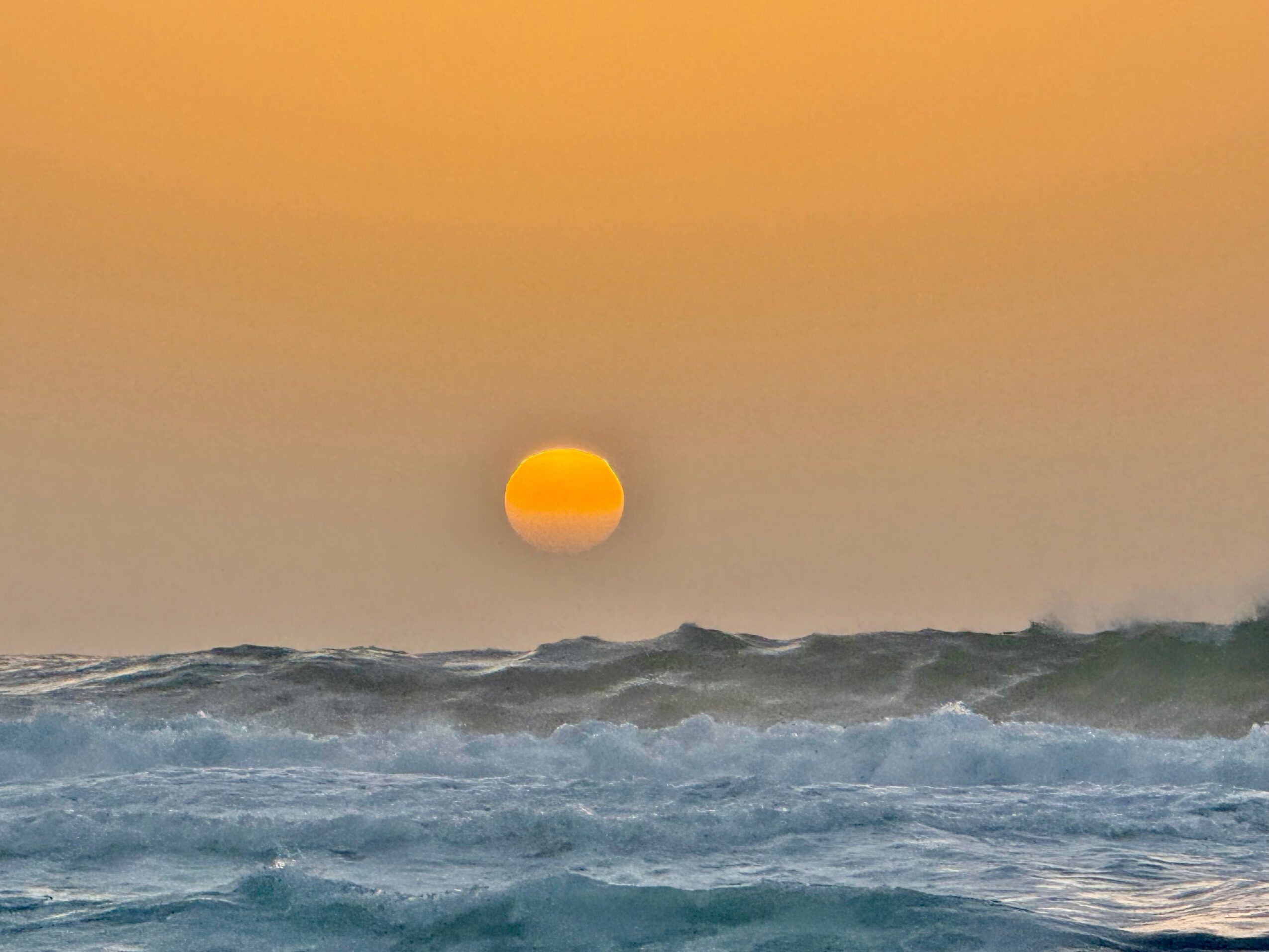 Sun setting over ocean waves with orange sky, calm water, and horizon line, peaceful scene, 20 words, alt_text_word_count: 20, confidence: 0.95