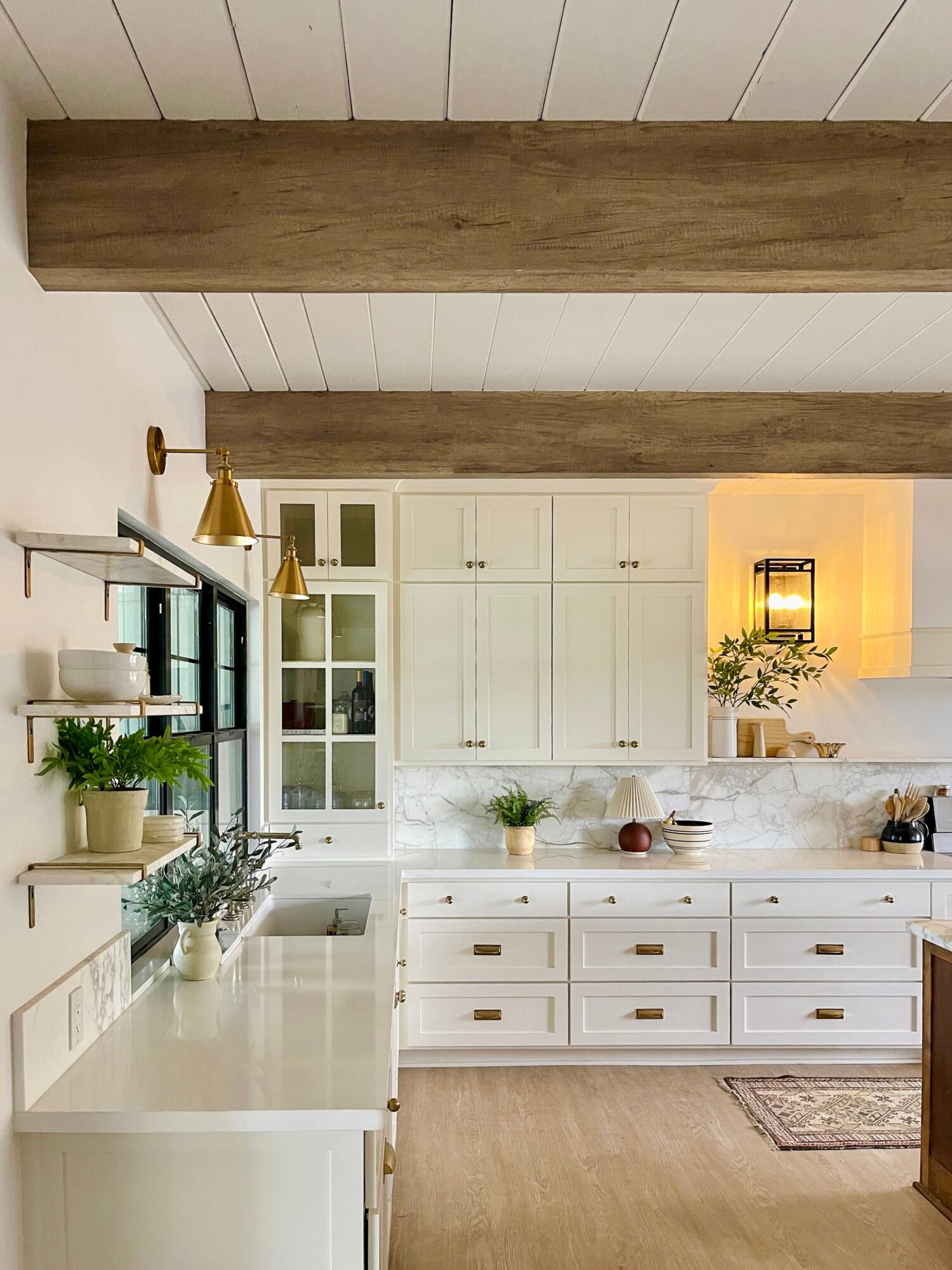 Kitchen with white cabinets, wooden beams, and a window with plants on the windowsill.