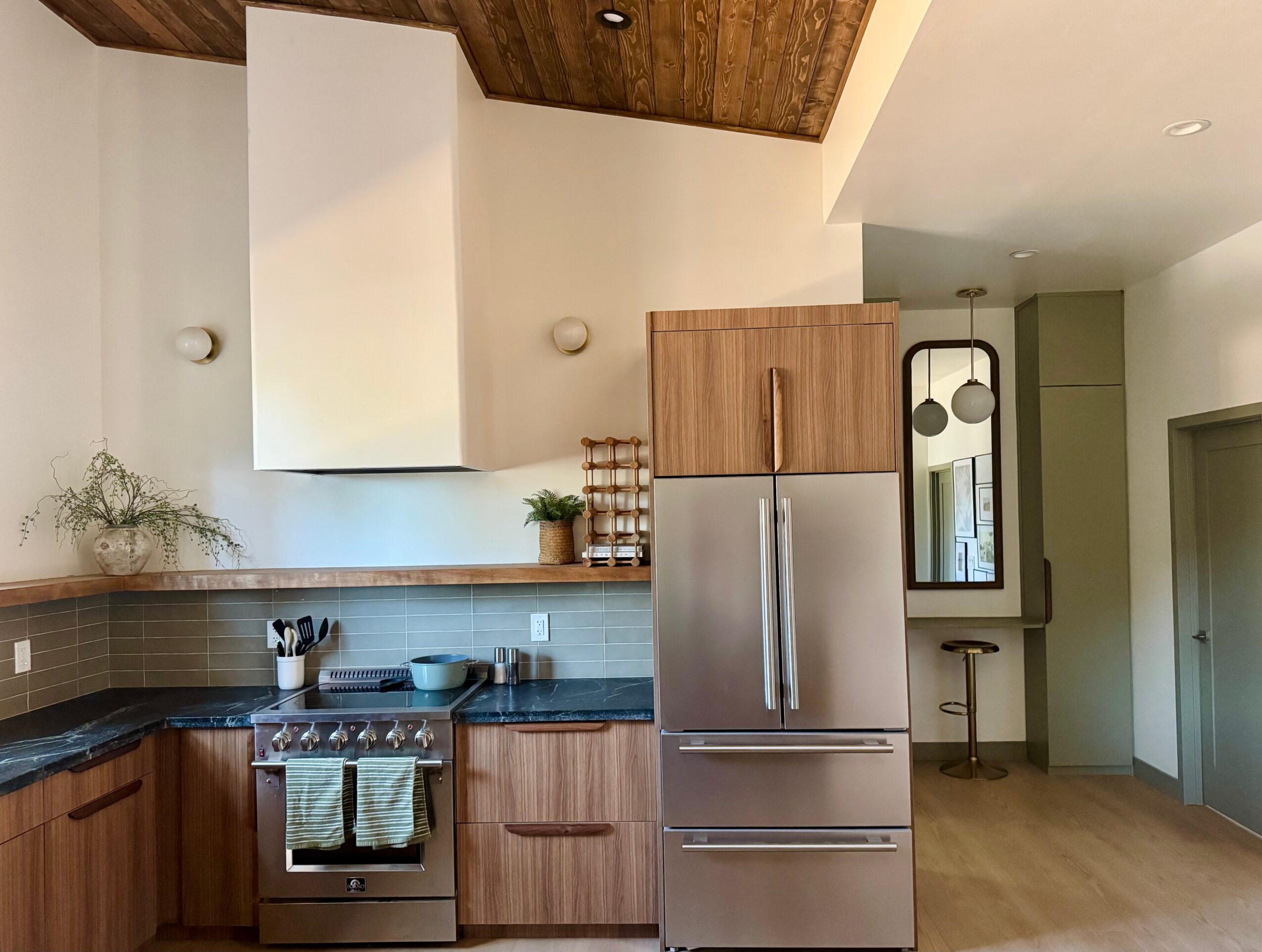 Kitchen with wooden cabinets, stainless steel refrigerator, and a stove with a towel hanging, ceiling with wood paneling, and a small bar area.
