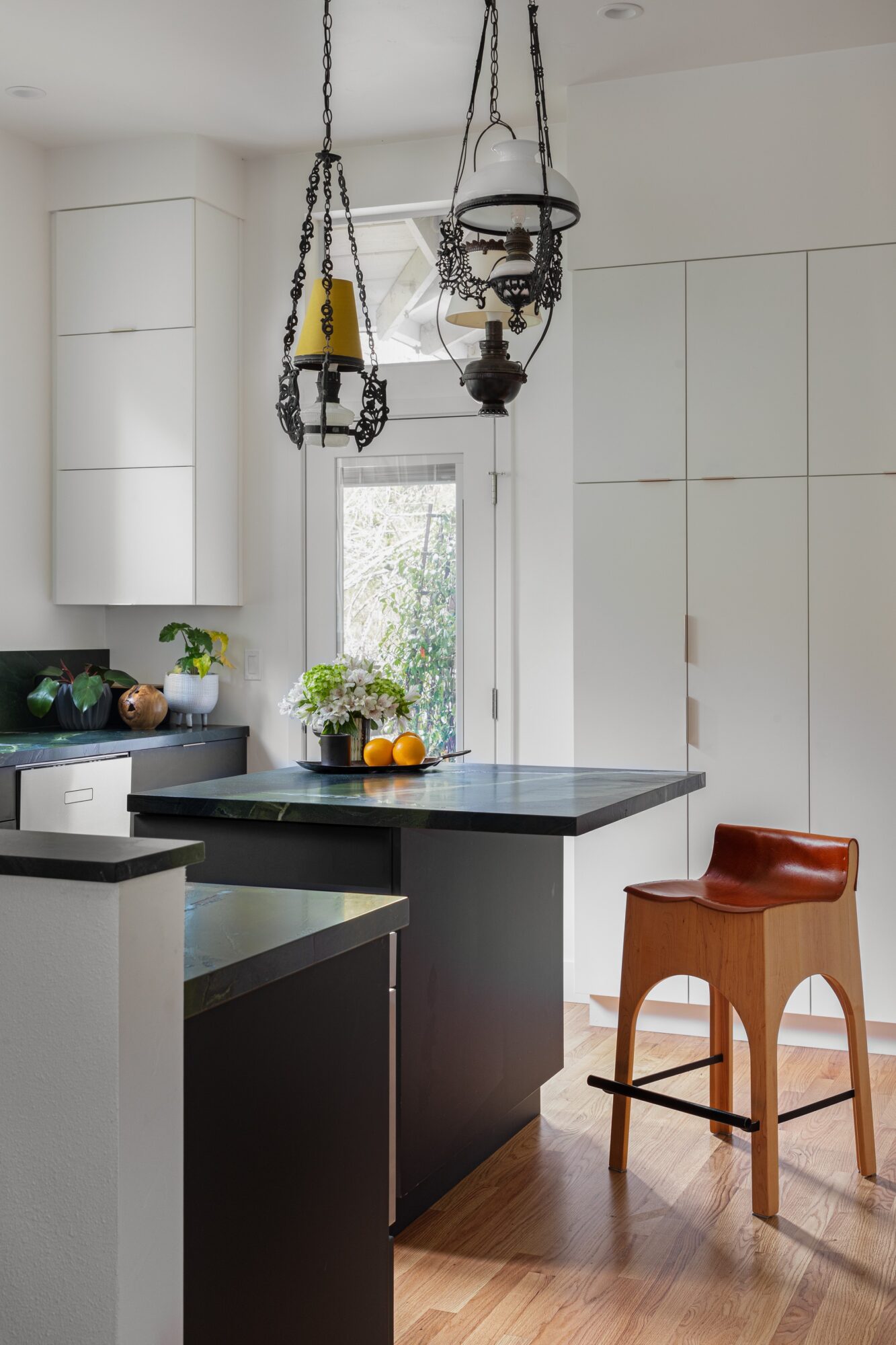 Kitchen with hanging pendant lights, white cabinets, a window, and a wooden chair with a brown cushion.