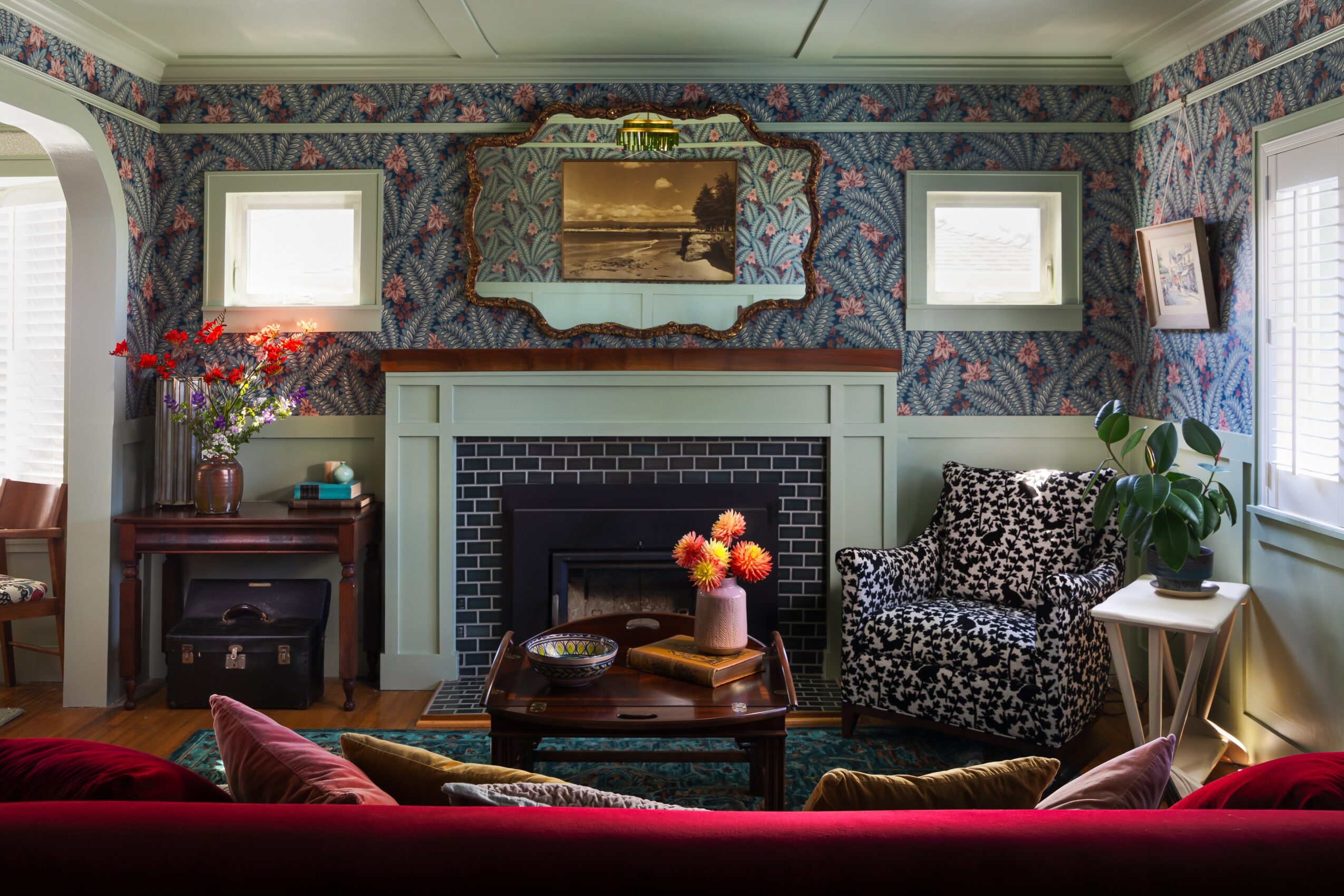 Living room with patterned wallpaper, a fireplace, a mirror, and various furniture including a floral armchair and side table.