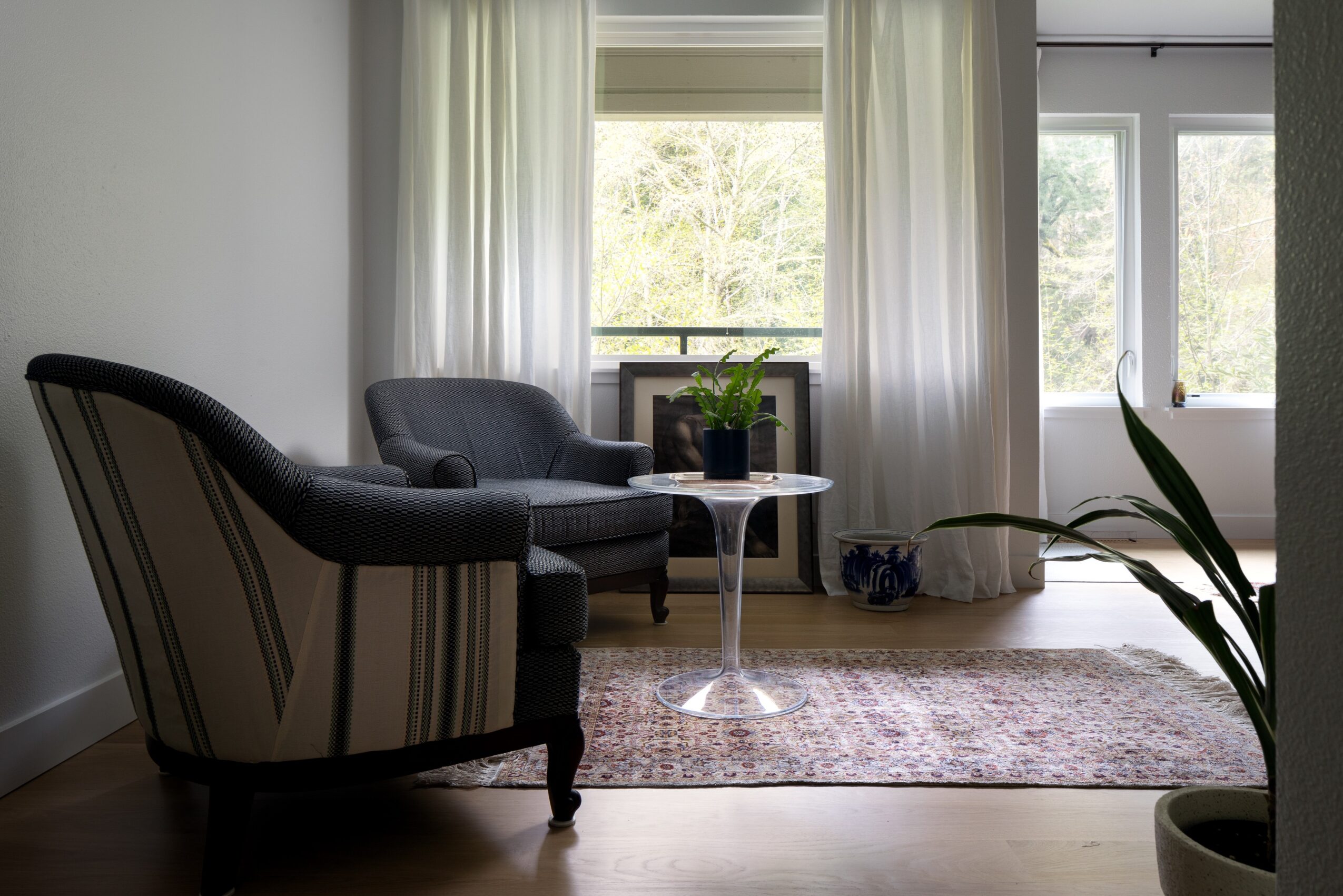 Living room with a dark sofa, striped armchair, small round table, and large window with curtains, natural light, and a rug.