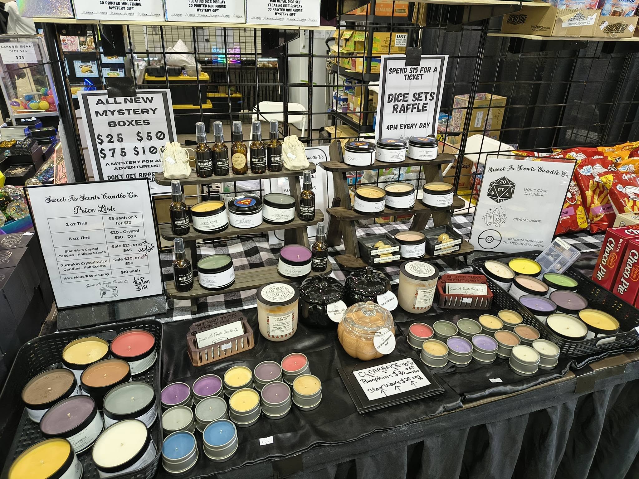 Display of various jars, containers, and boxes of food items on a table at a market stall, with signs and packaging visible.