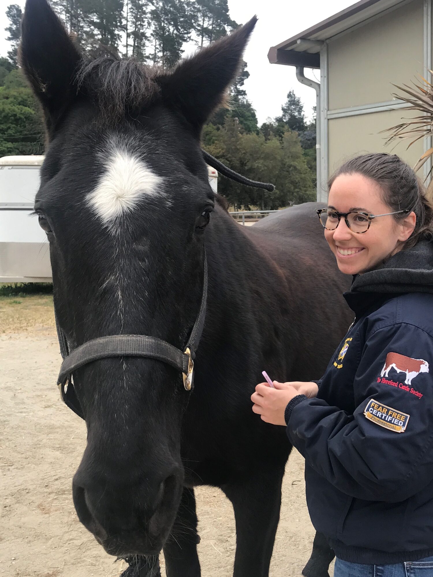 Person in uniform smiling next to a black and white horse outdoors.