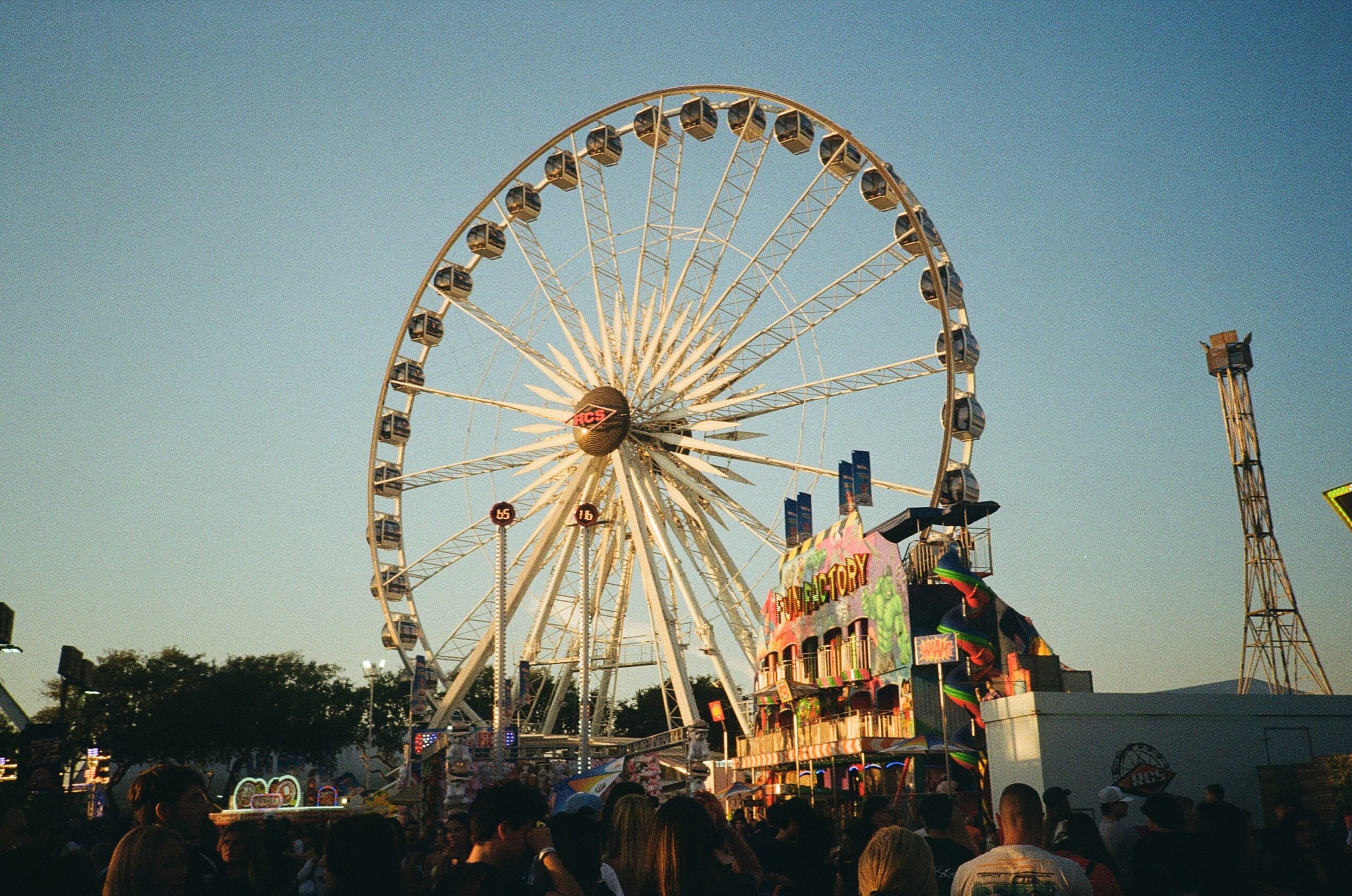 Ferris wheel and carnival rides with a crowd of people at an outdoor fair during daytime.