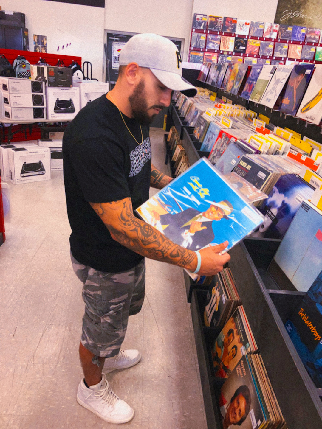 Man with a white cap and tattoos on his arm browsing vinyl records in a store.