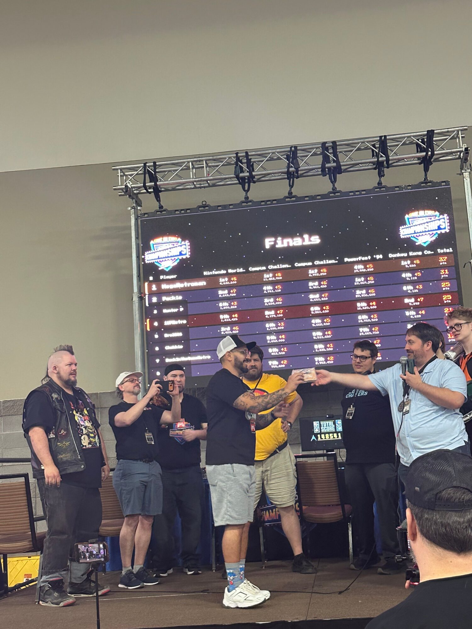 Group of people standing in front of a large screen displaying a list of names and logos, some holding trophies or awards.