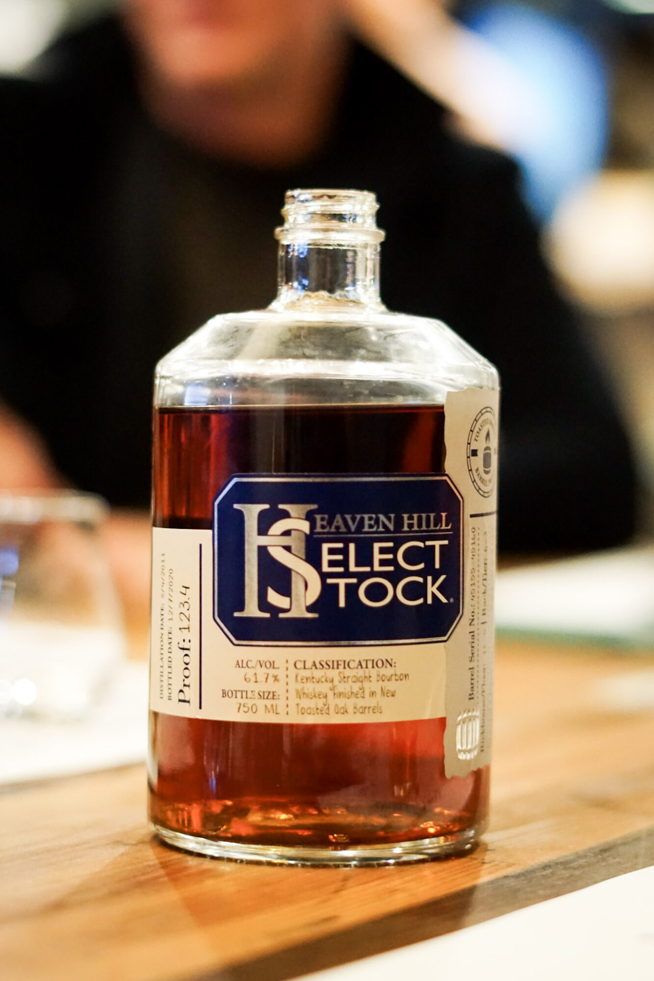 Bottle of bourbon whiskey on a wooden table with a blurred person in the background.
