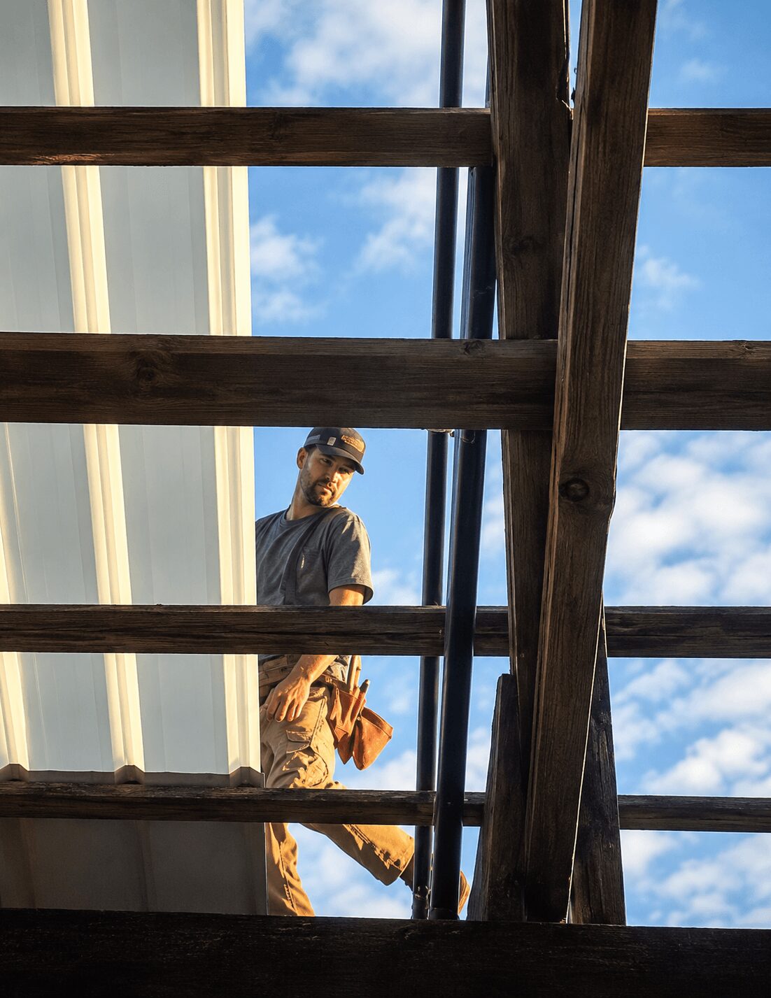 Person standing on wooden structure holding a yellow power tool, sky with clouds in background.
