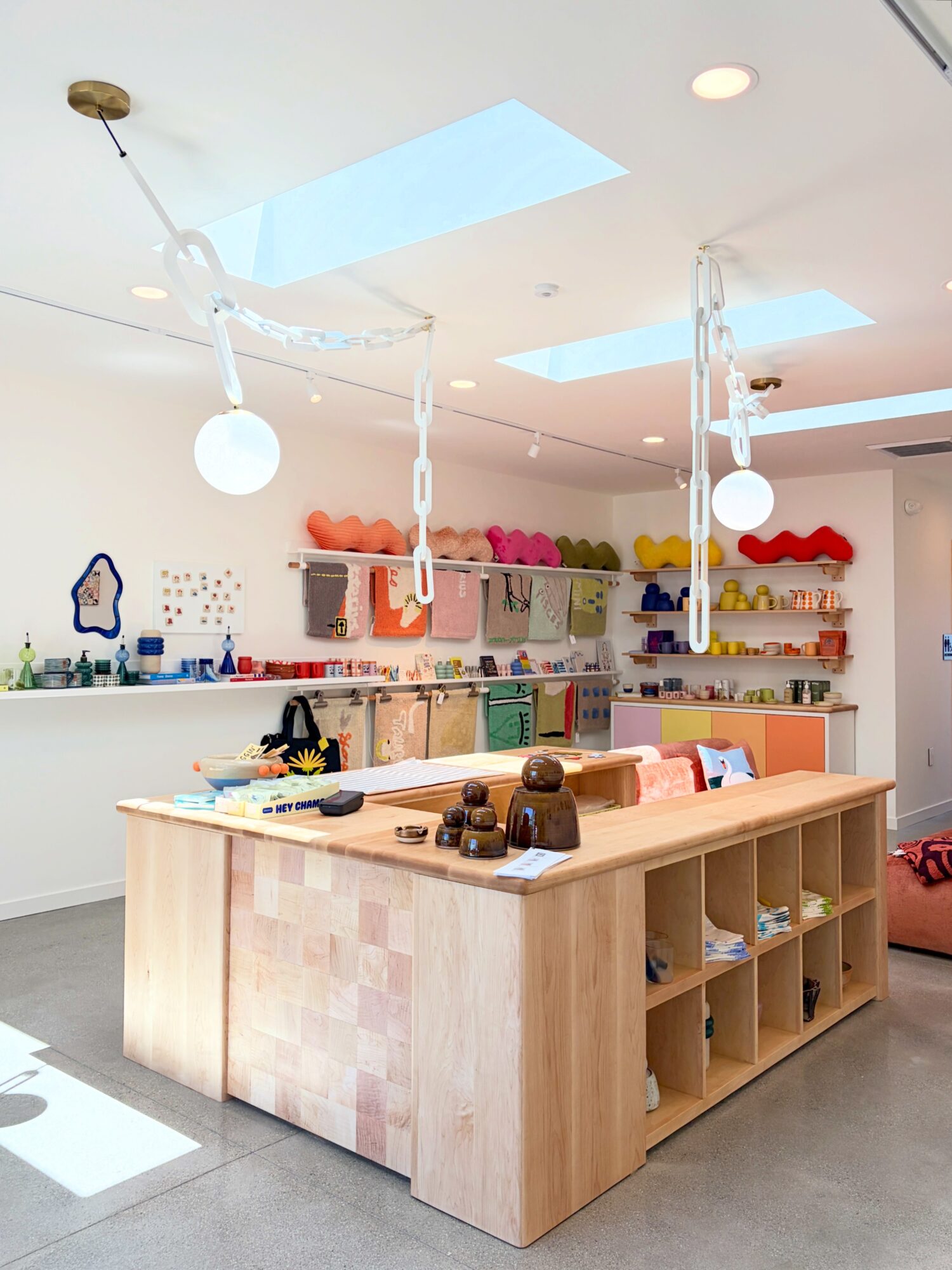 Bright, modern store interior with wooden display table, colorful hats on shelves, and skylights overhead.