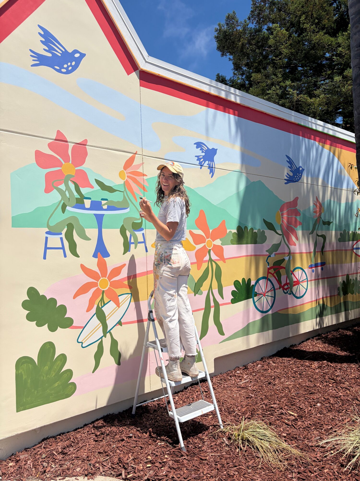 Person standing on a white platform in front of a colorful mural with flowers, animals, and mountains.