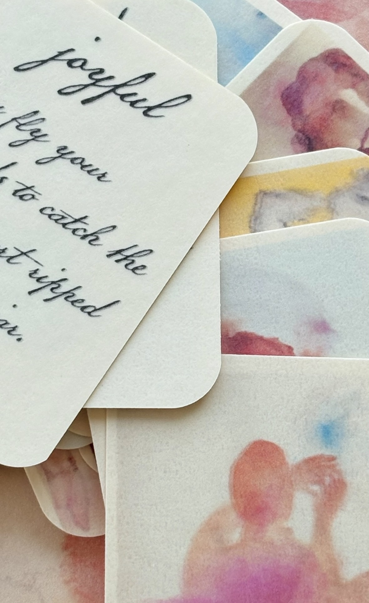 Close-up of handwritten notes and watercolor paintings on paper, with a person holding the papers. Bright colors and soft focus.
