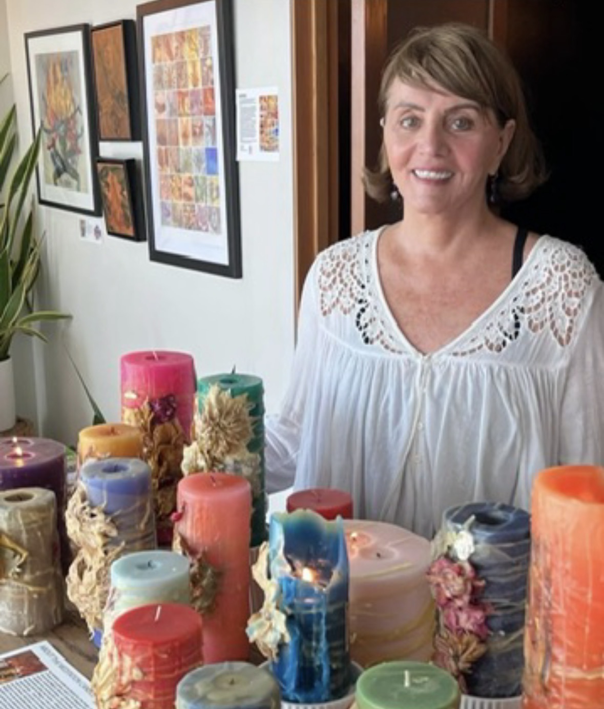 Woman standing indoors near colorful candles and artwork on the wall, smiling at the camera.